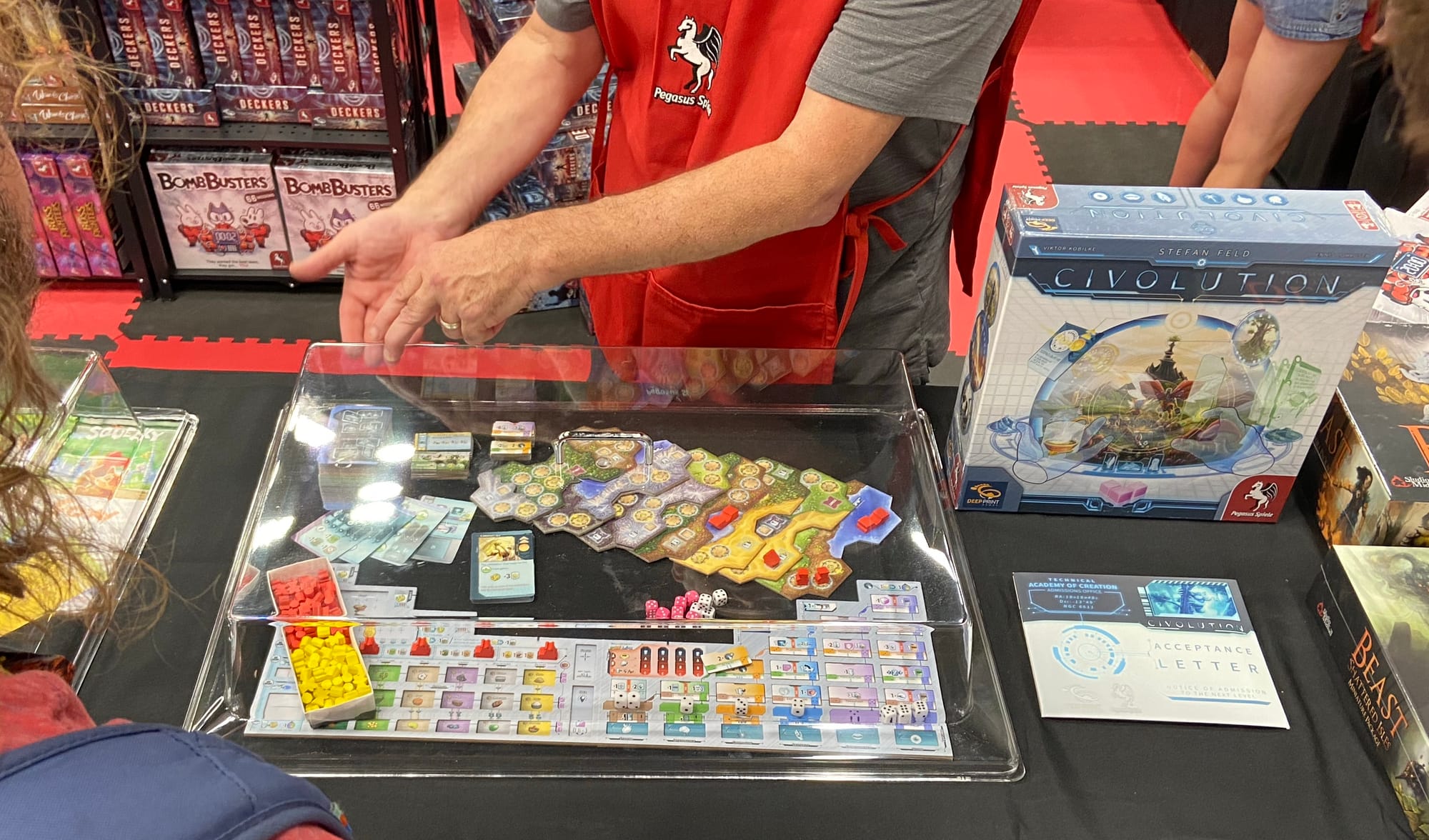 The game Civolution is on a table next to some of its components covered by a plastic shield.