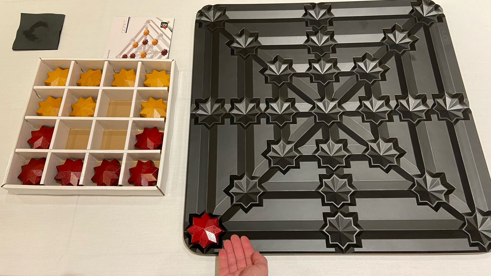 A giant wooden playing board about two feet square has a wooden star in an indentation, with other wooden stars in boxes on the table. 