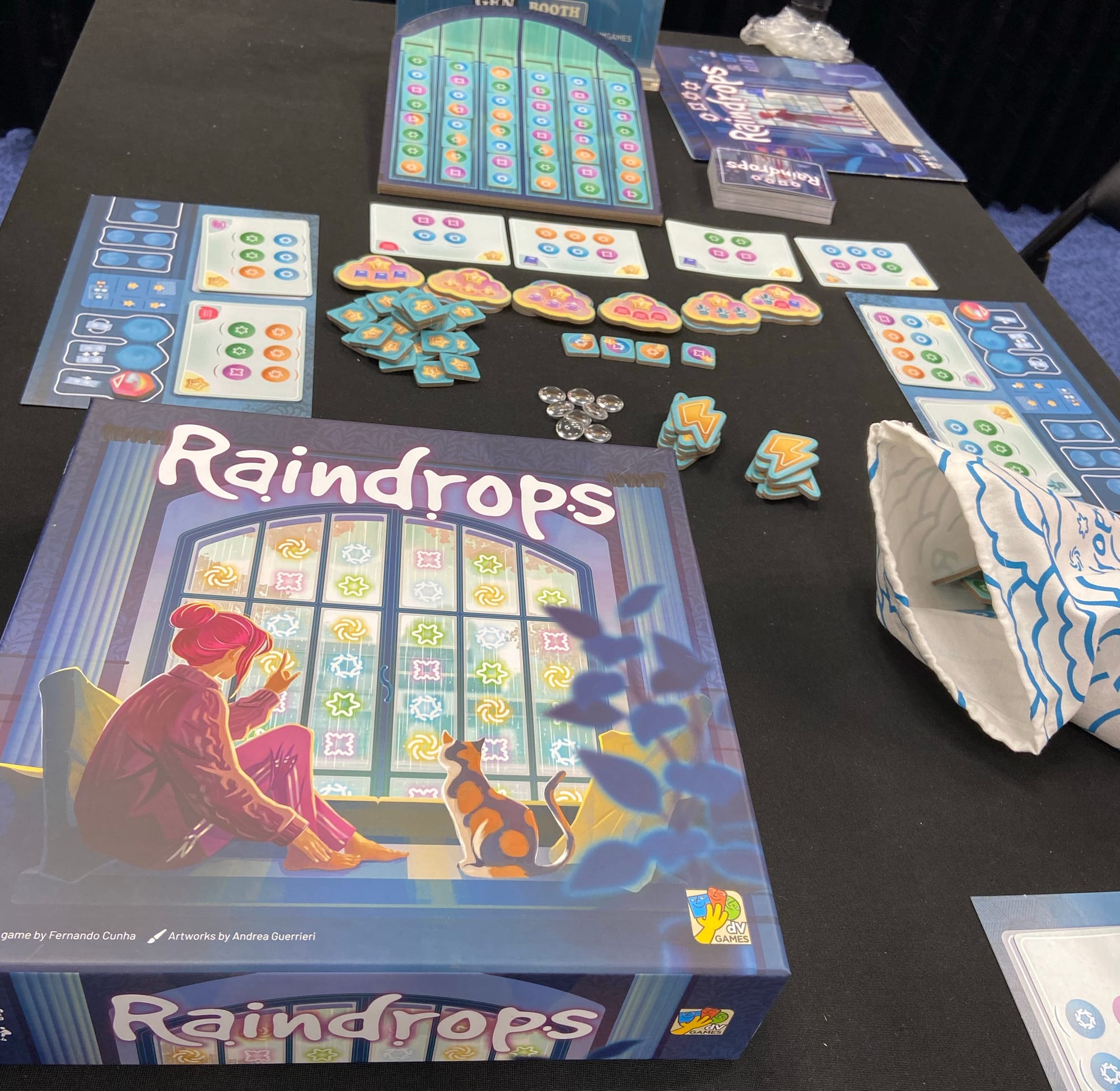 The box of Raindrops next to the components, which primarily consists of a tilted game board covered with domino-style tiles.