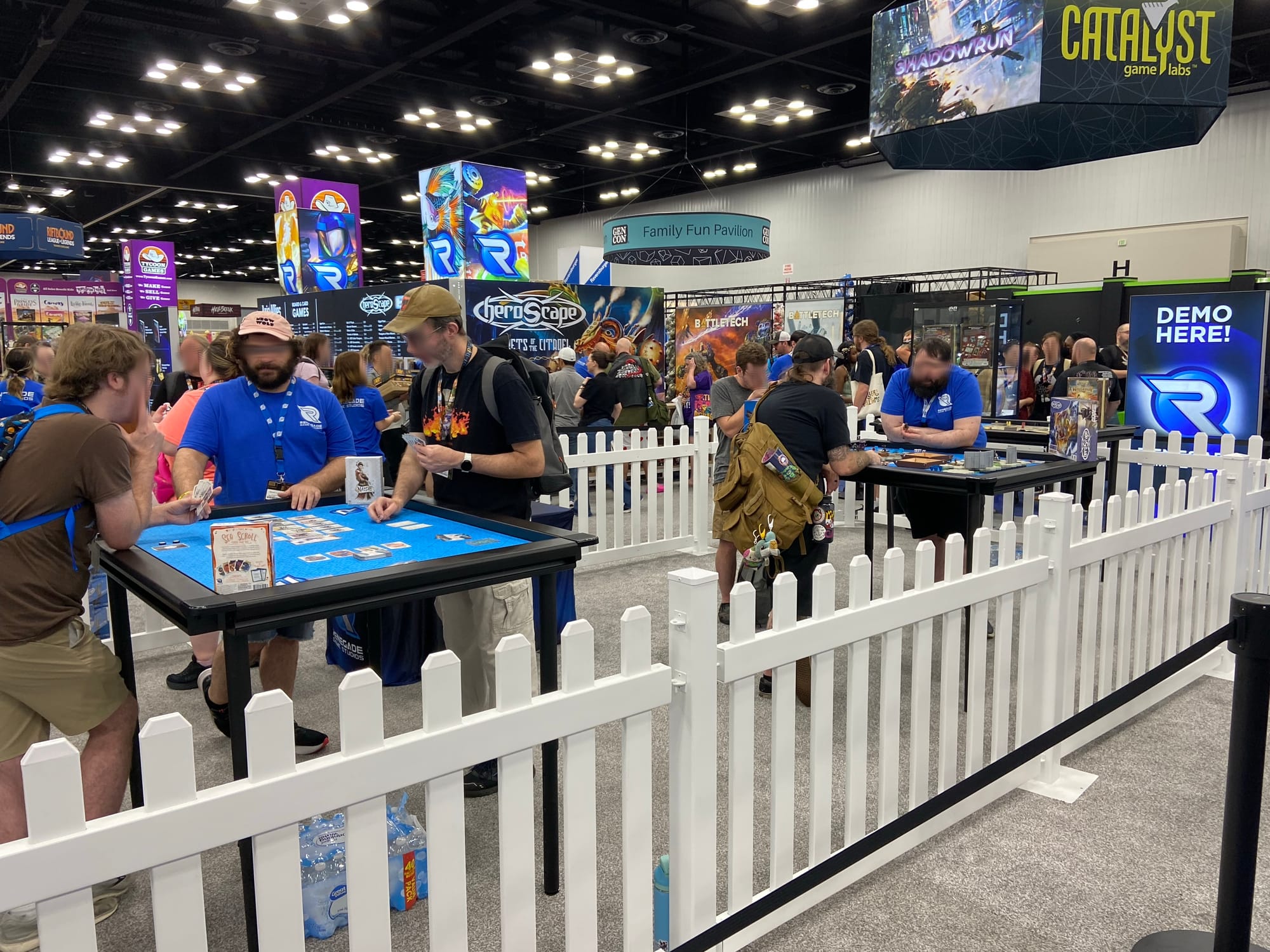 A white picket fence in the Renegade Game Studios booth surrounds demo tables and players.
