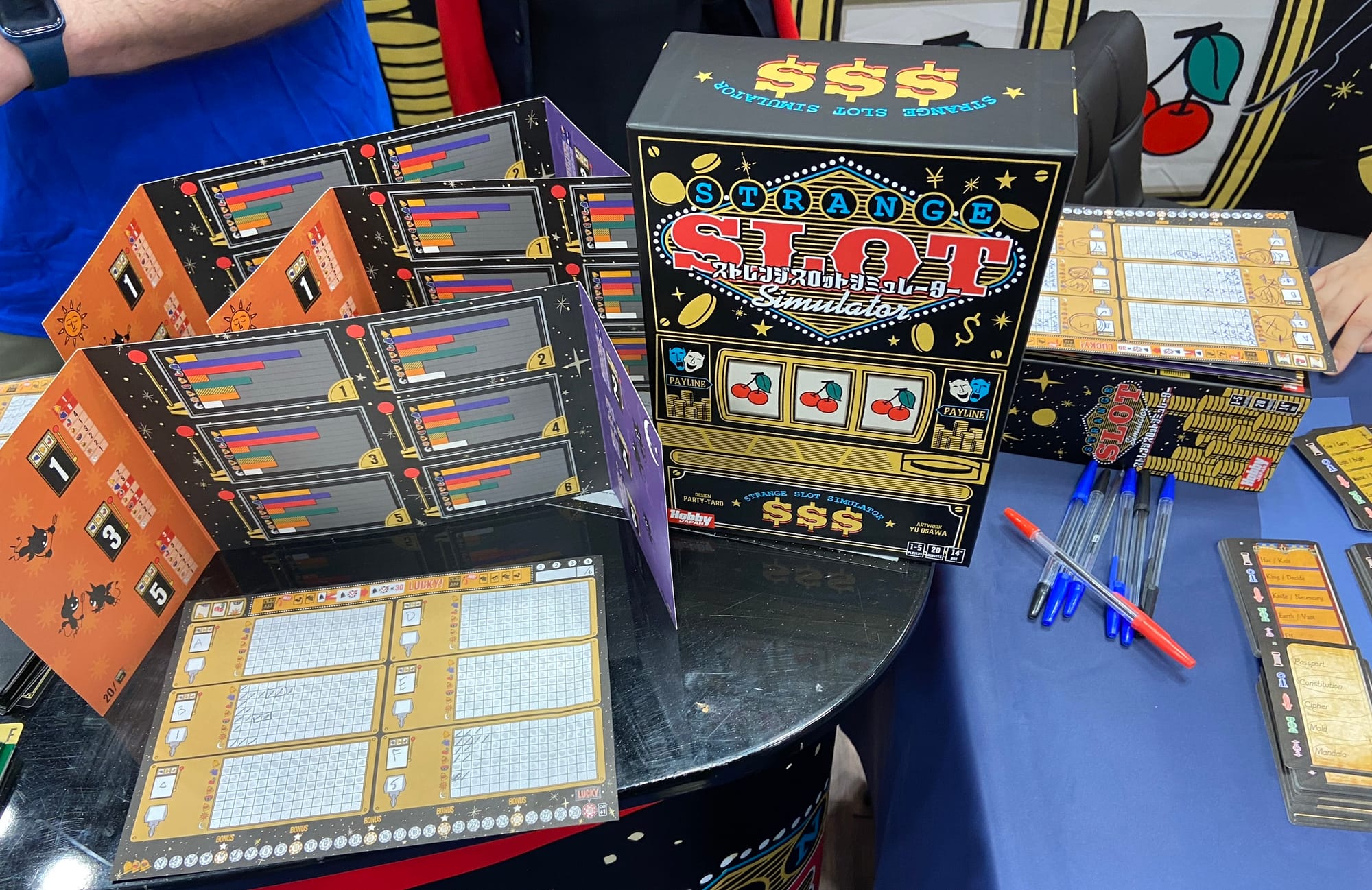 The box for Strange Slot Simulator stands next to player screens, note pads, and pens.