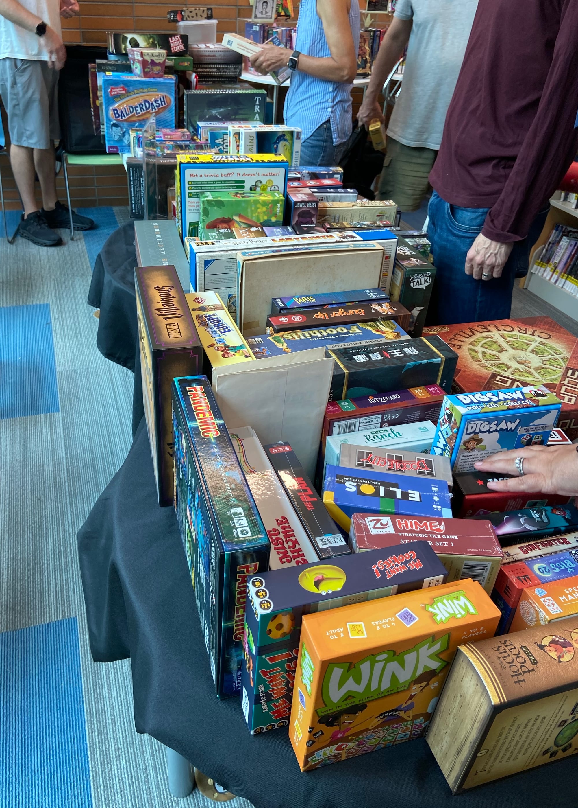 Tables in a line have 150+ games on them, and folks are standing next to the tables and checking out the selection.