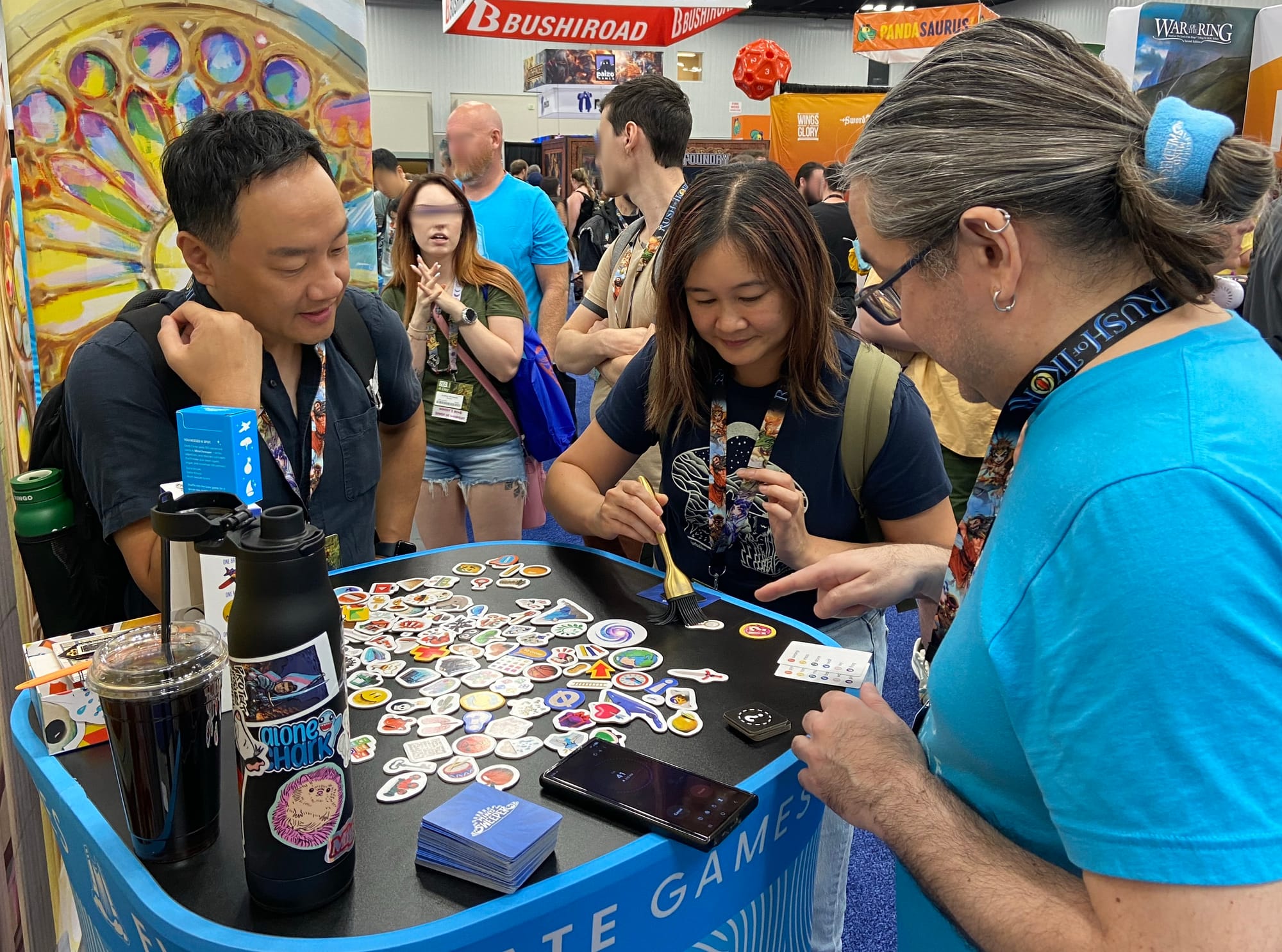 A woman uses a tiny broom to sweep game pieces around a small table while a timer counts down on a phone.