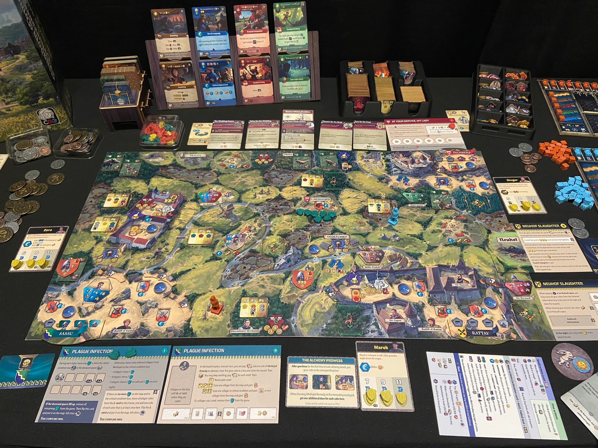 A game board shows a countryside landscape and is surrounded by cards, cubes, coins, and tiles.
