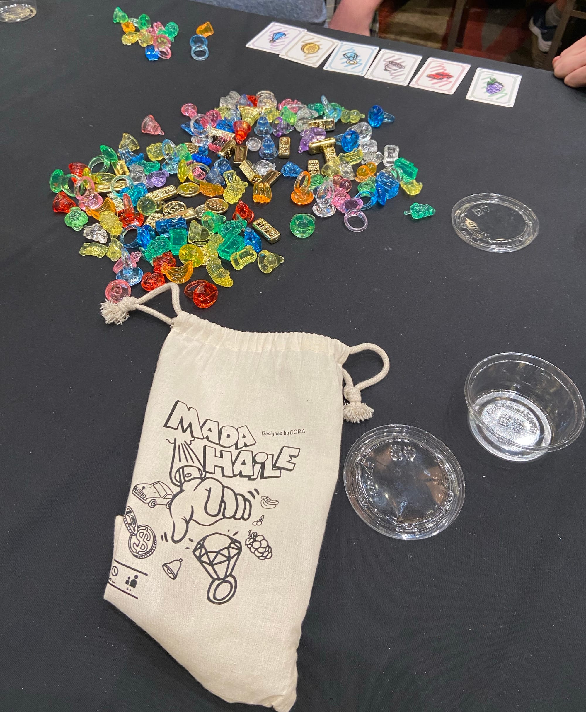A pile of plastic and metal bits in various colors are next to a cloth bag labeled MADA HAiLE.