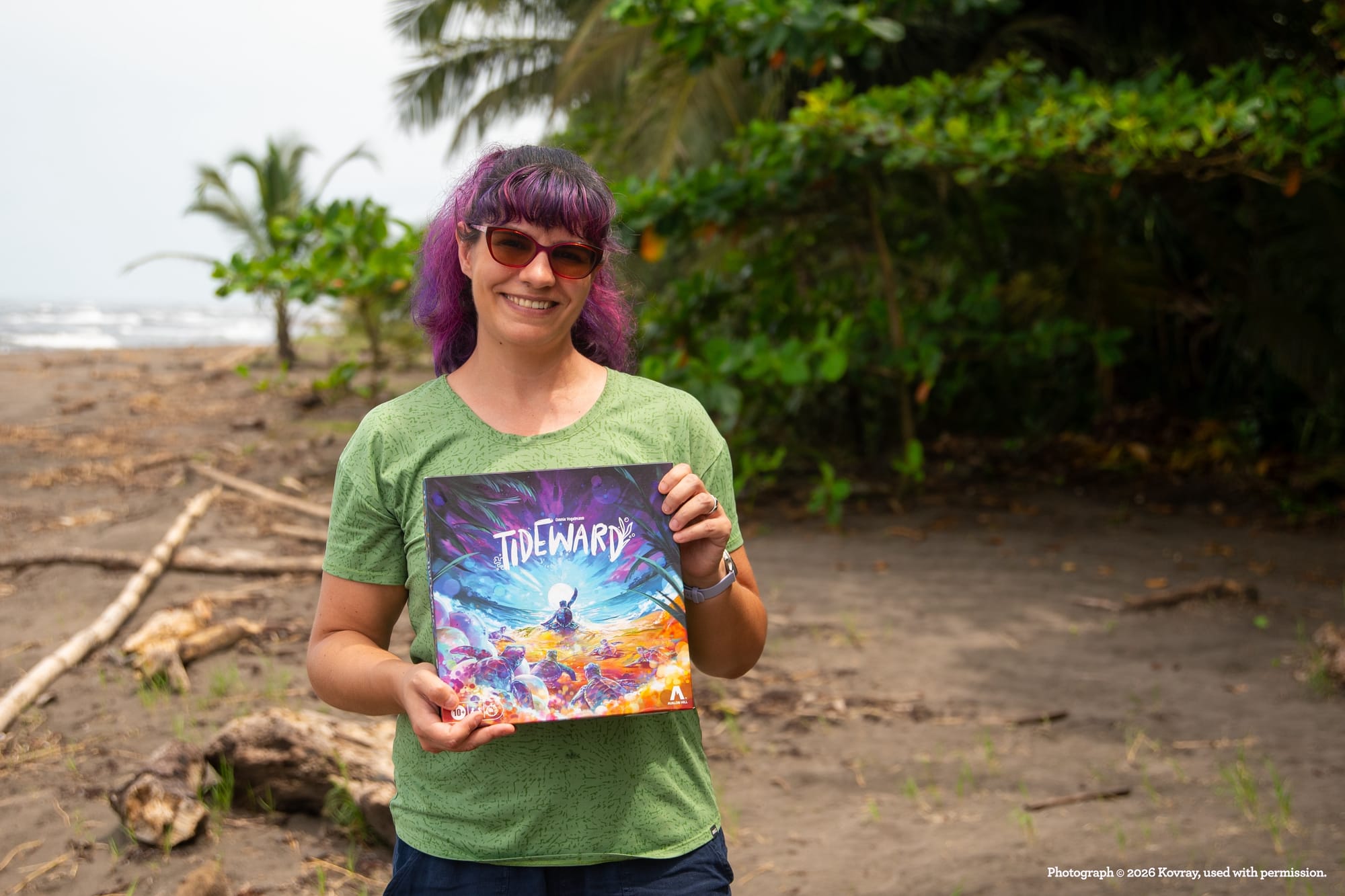 A woman holds the Tideward game box in a tropical-ish location.
