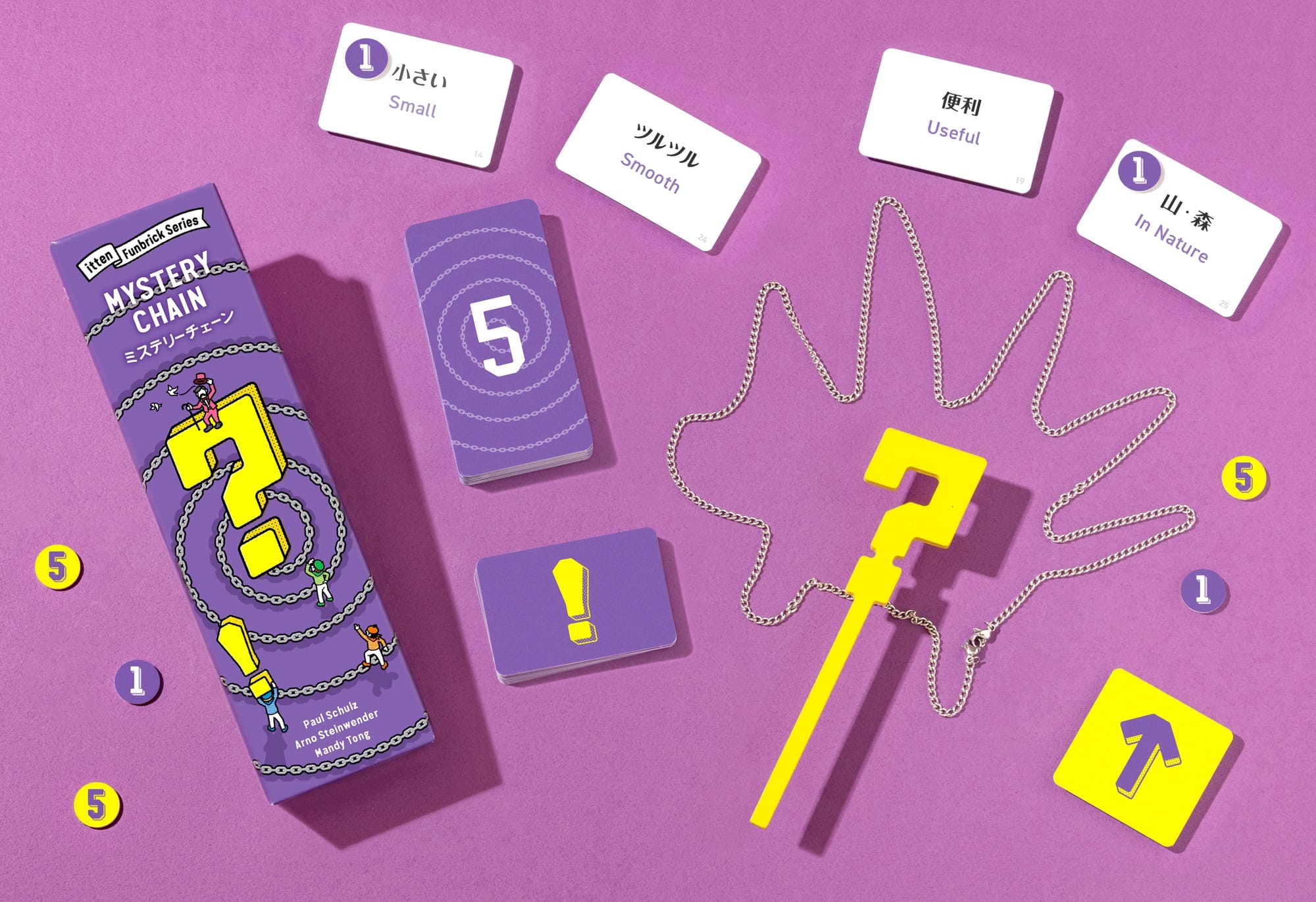 A linked chain lies on a table in the shape of a hedgehog, with a wooden stick bearing a question mark at top being placed on top of the chain. Cards with English and Japanese words on them are nearby, some of which bear 1-point tokens.