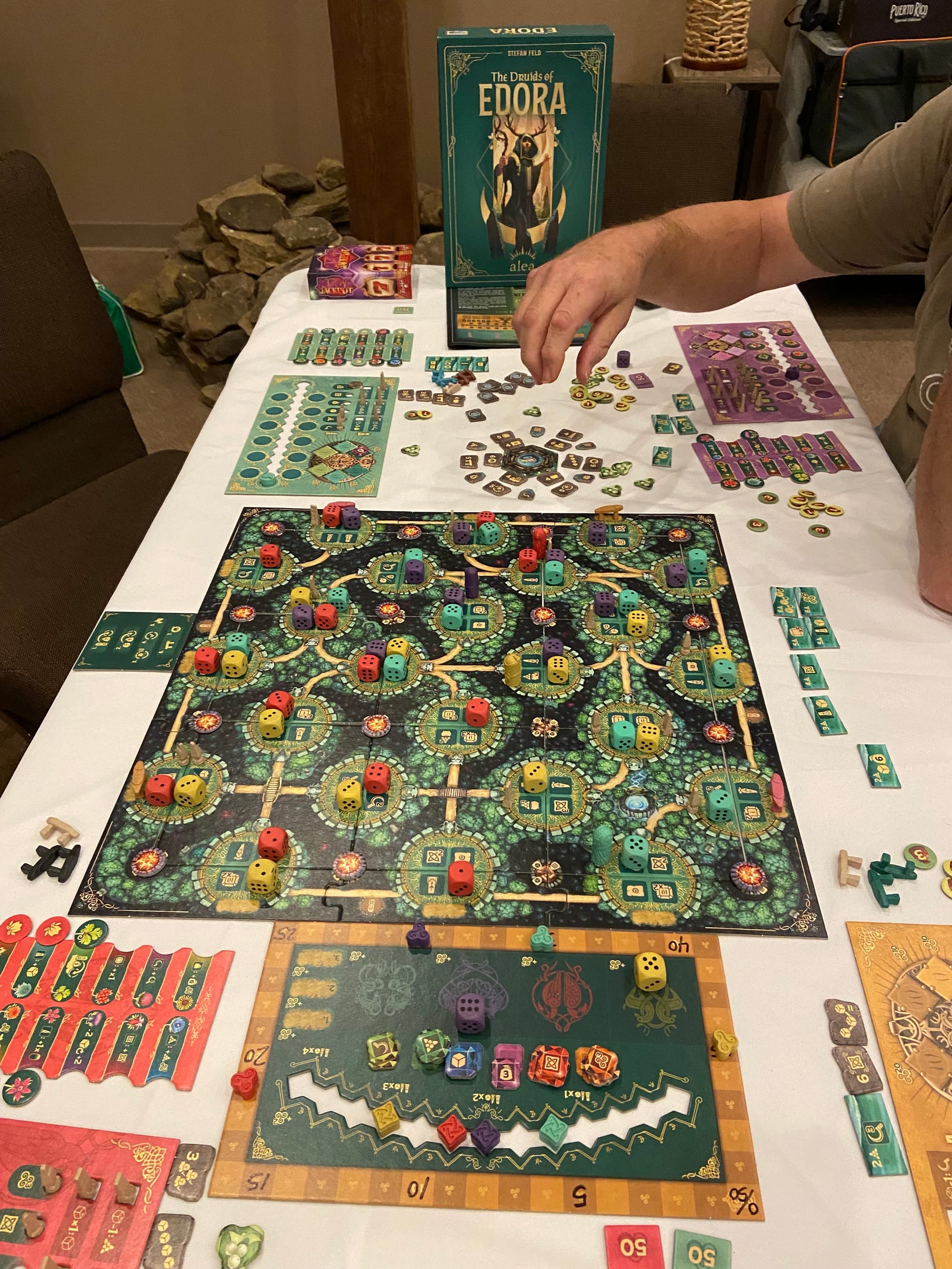 A mid-game shot of The Druids of Edora, with a player's hand hovering above the game board.