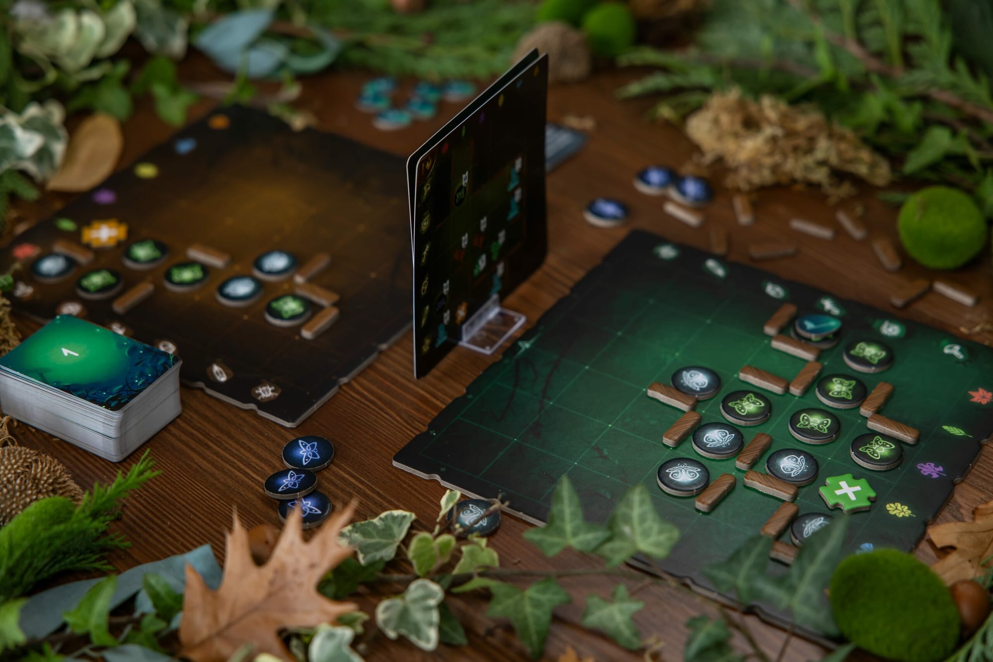 Two 6x6 playing areas face one another, with vertical maps in a card holder between the playing areas. The boards shows firefly tokens and obstacles. A deck of cards is nearby.