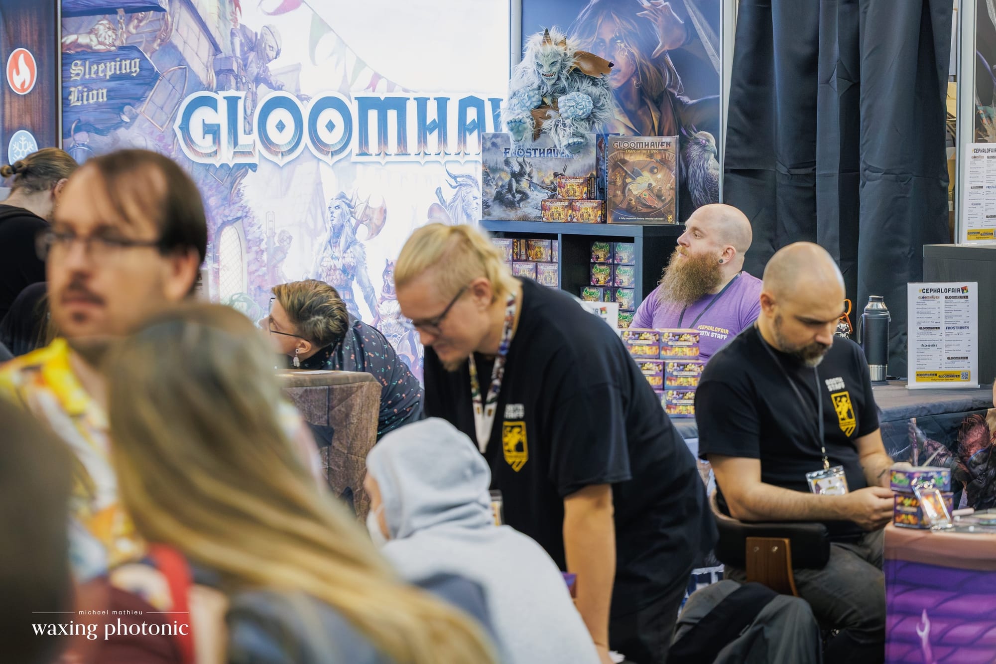 The Cephalofair booth at SPIEL Essen 26, with customers in the foreground, an employee teaching a game in the middle distance, and other employees in the background.