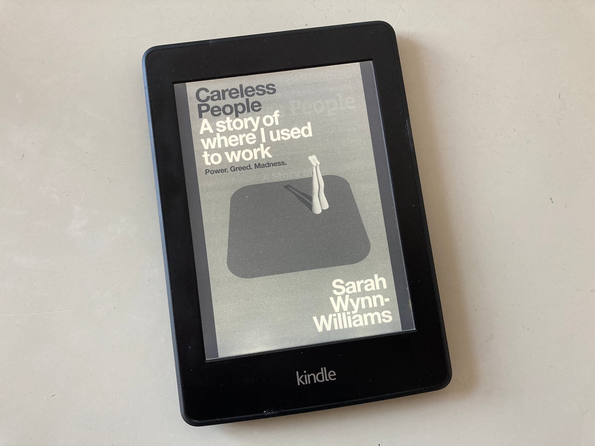 A Kindle on a grey desktop shows the monochrome cover of Careless People.