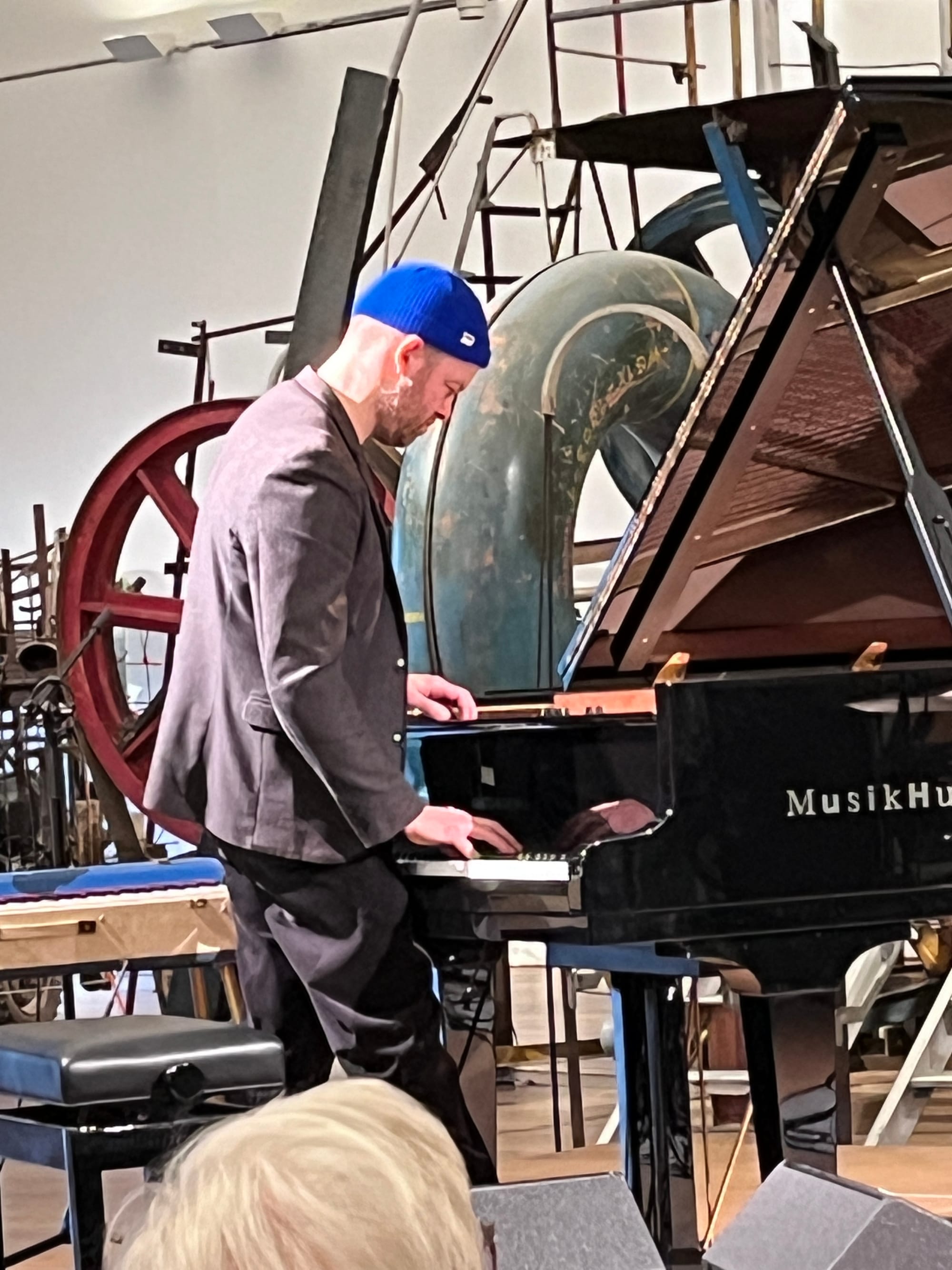 A man in a blue hat stands at a piano