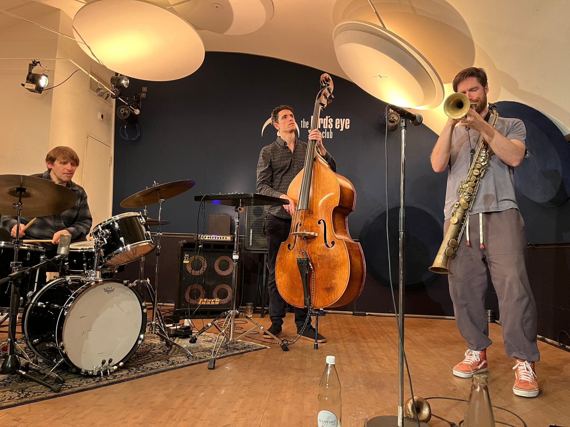 A drummer, a bassist, and a trumpet player also holding a saxophone