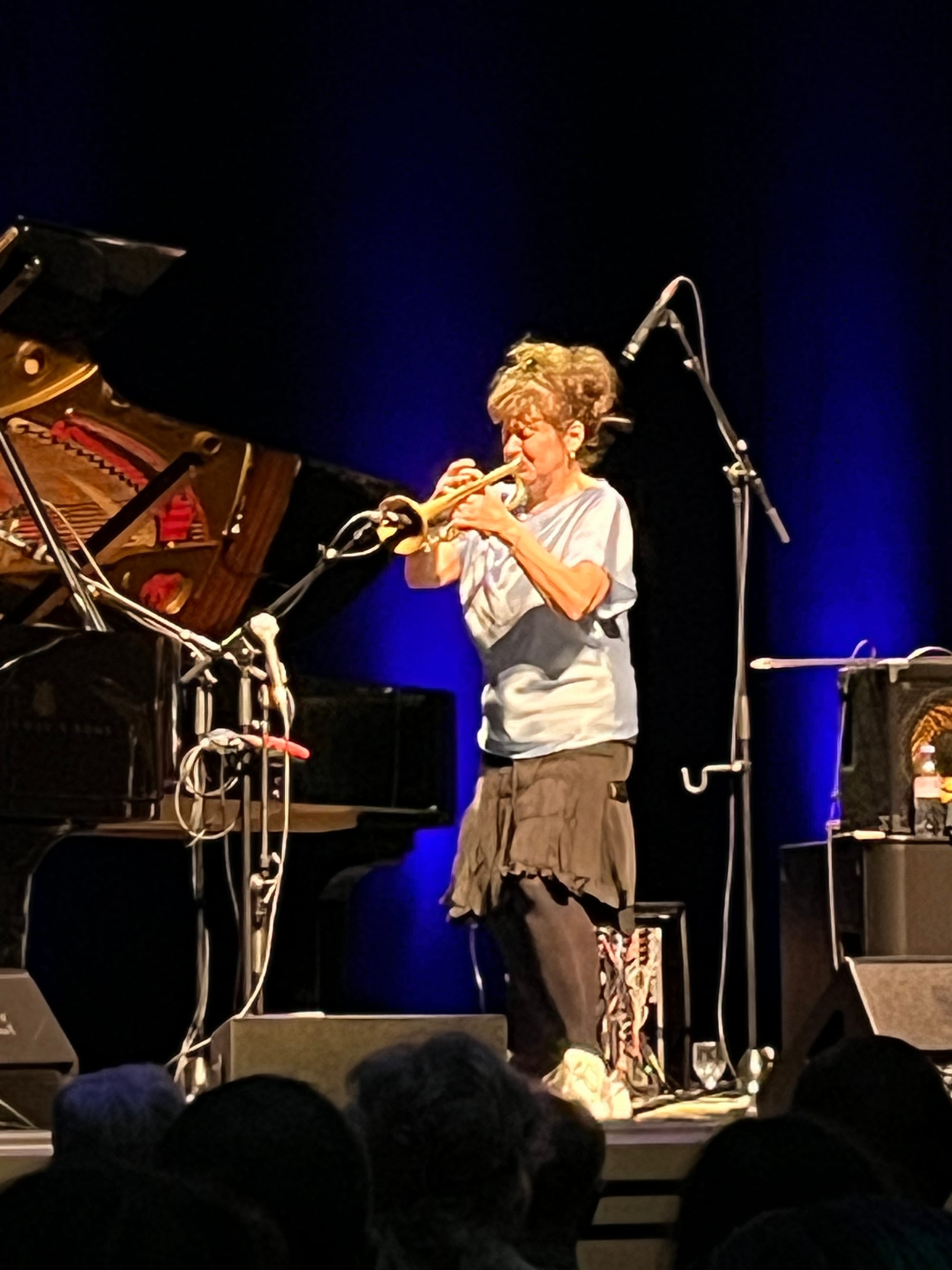 A woman in a silvery shirt plays the trumpet