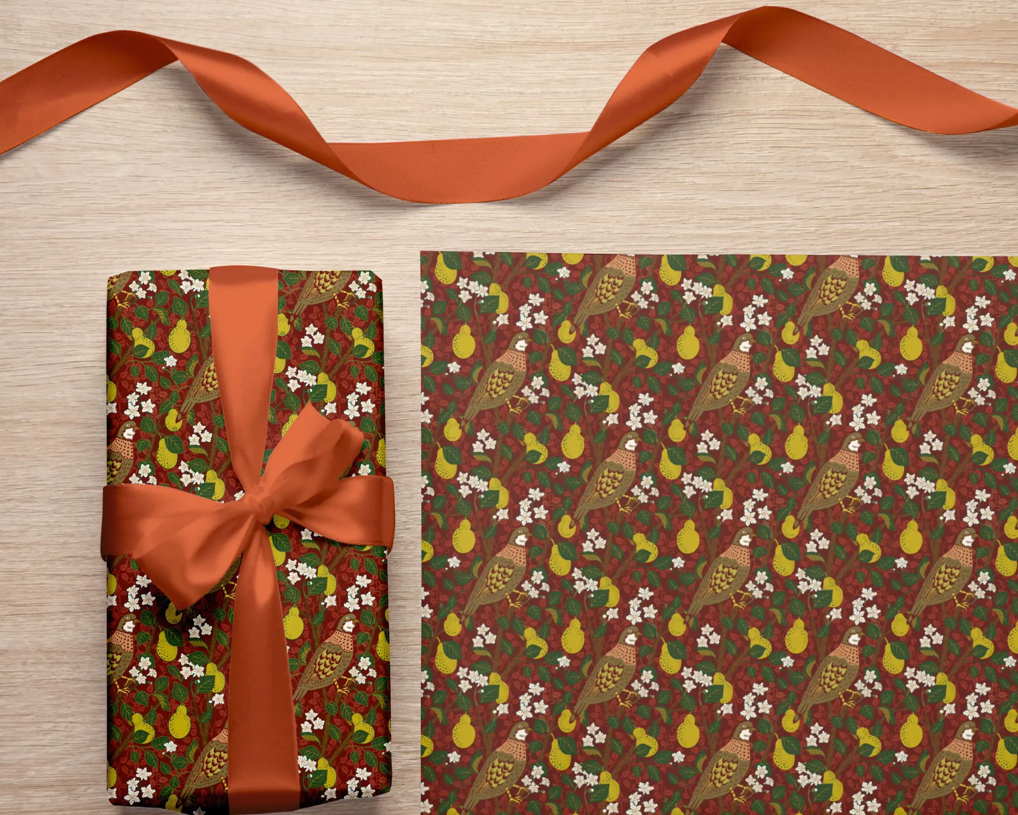 A parcel tied with an orange ribbon, beside a sheet of wrapping paper printed with partridges among pears and white blossom, on a deep red ground.