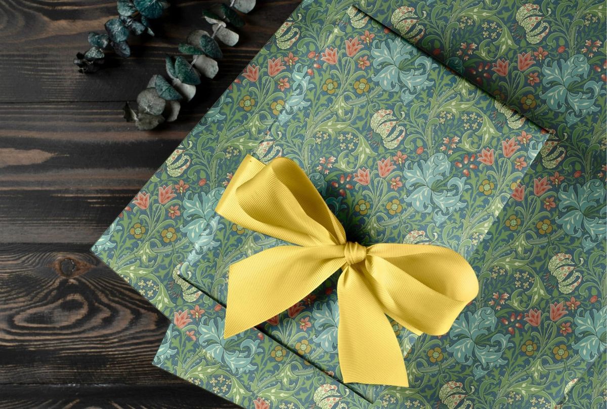 Golden Lily wrapping paper, pale blue lilies and coral flowers on a dark blue ground, tied with a yellow bow on dark wood.