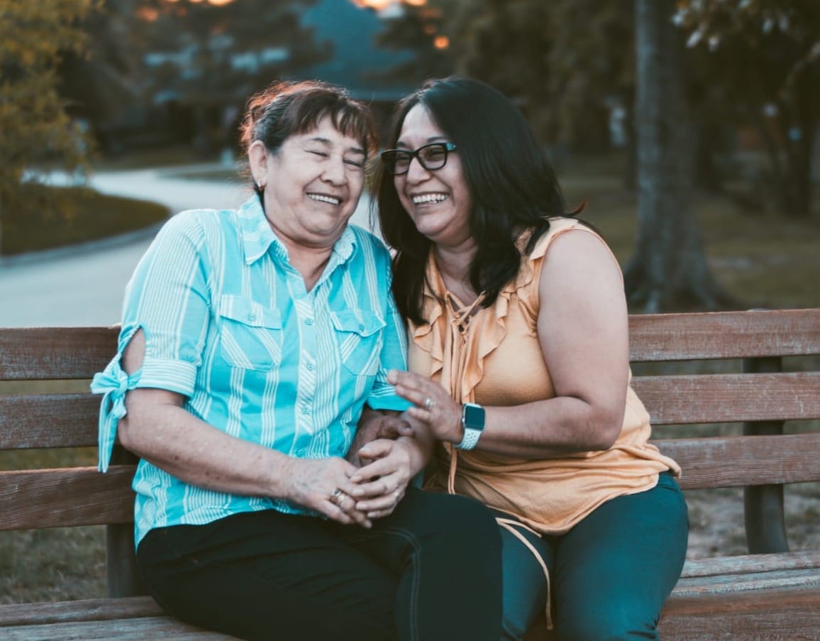 Two women sitting on a bench laughing.