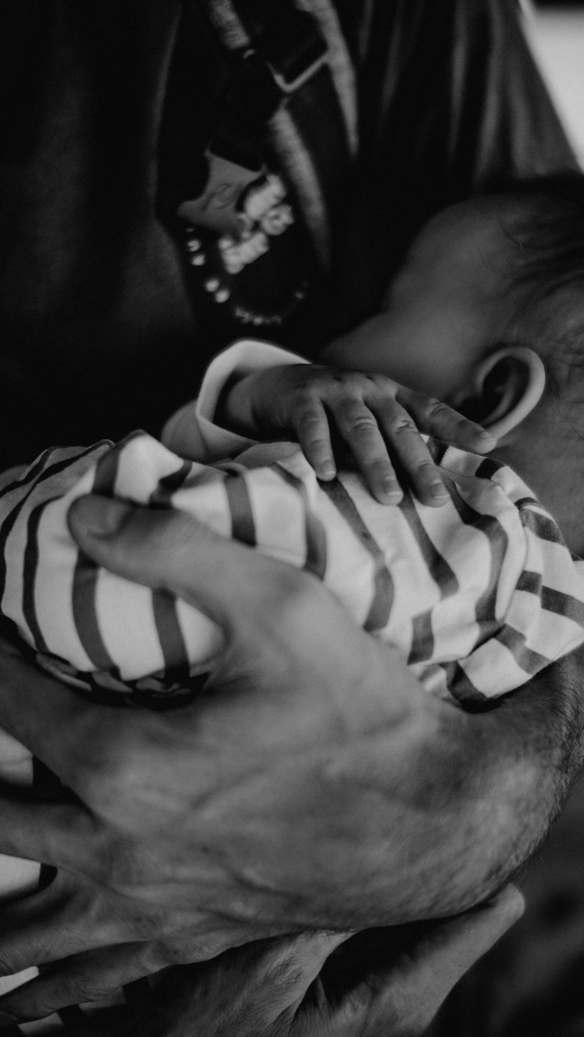 A baby being held close, perhaps by a man; focus of the photo is on the man's and baby's hands.