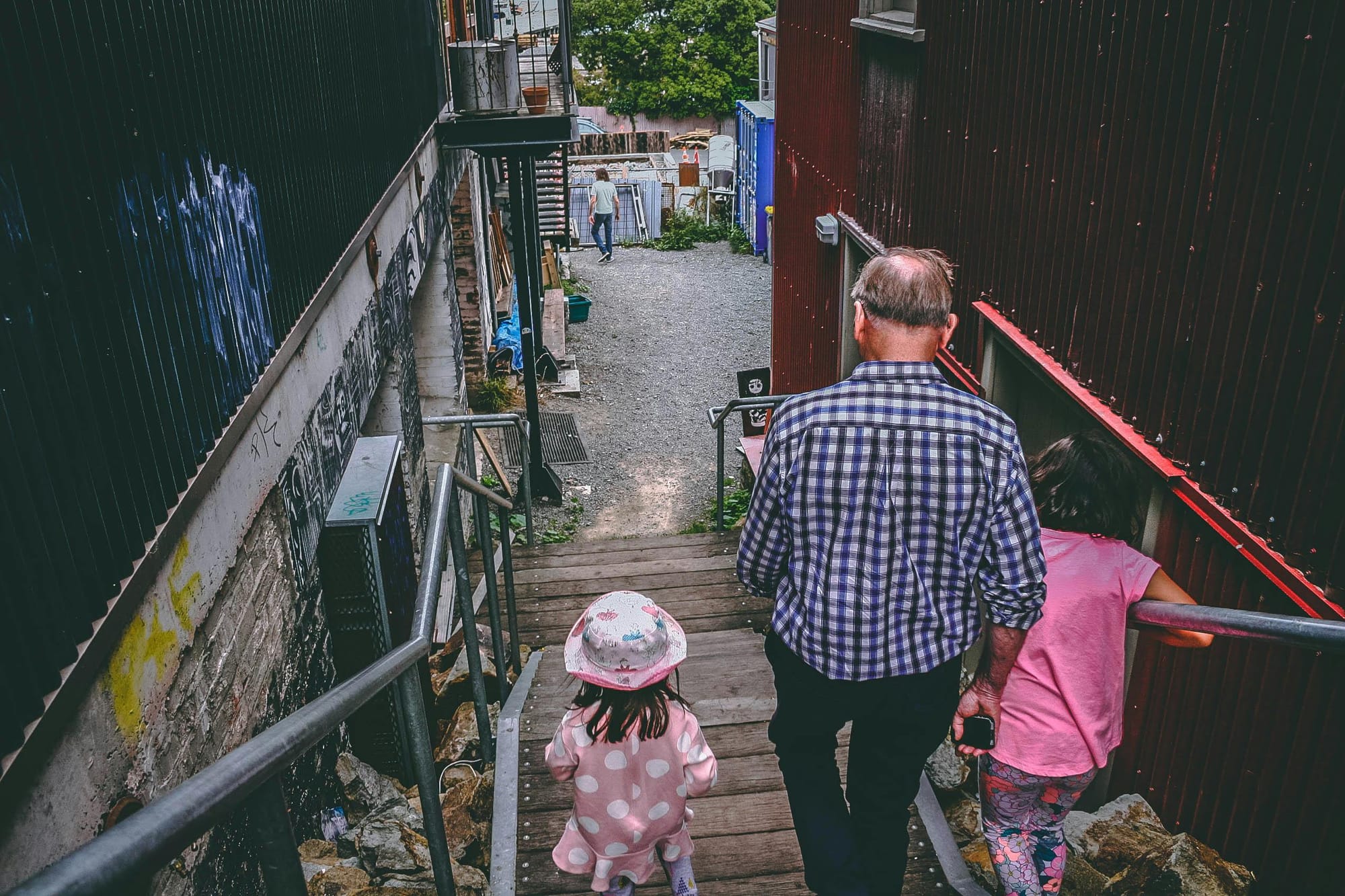 A man and two girls walk down wooden steps between two buildings.