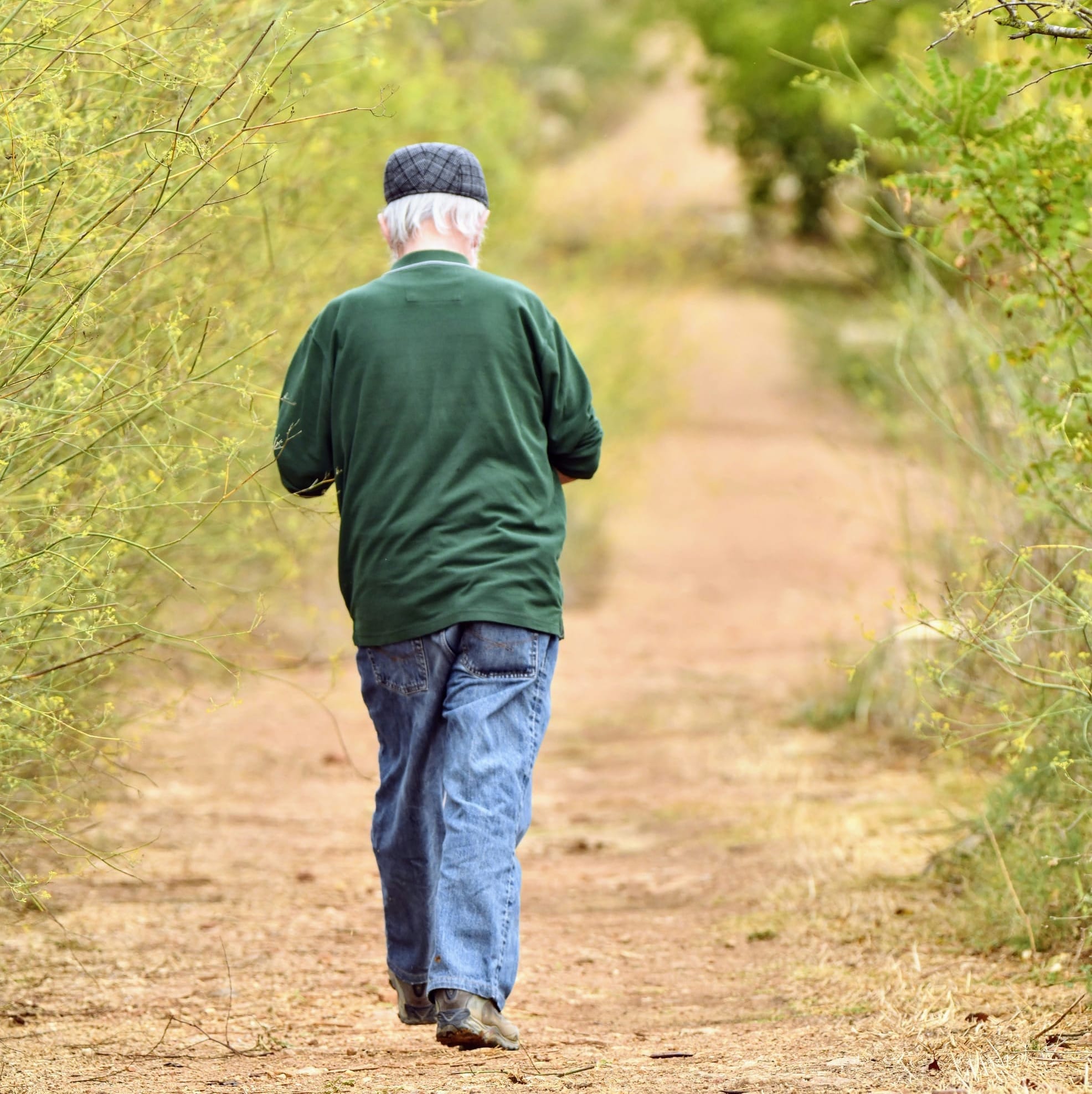 An older man walks along a wide dirt path.