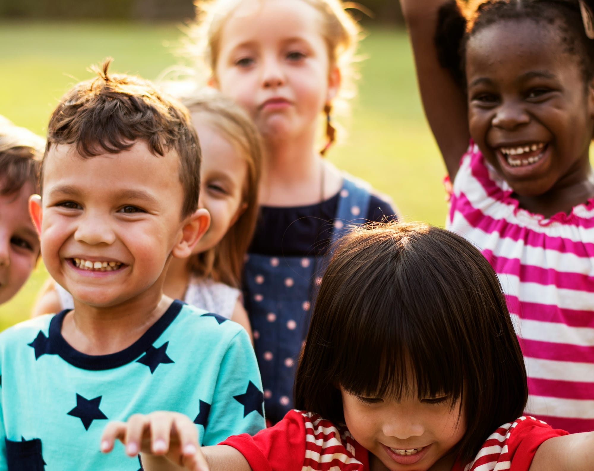 A group of children outdoors in warm sunshine, almost all smiling happily. 