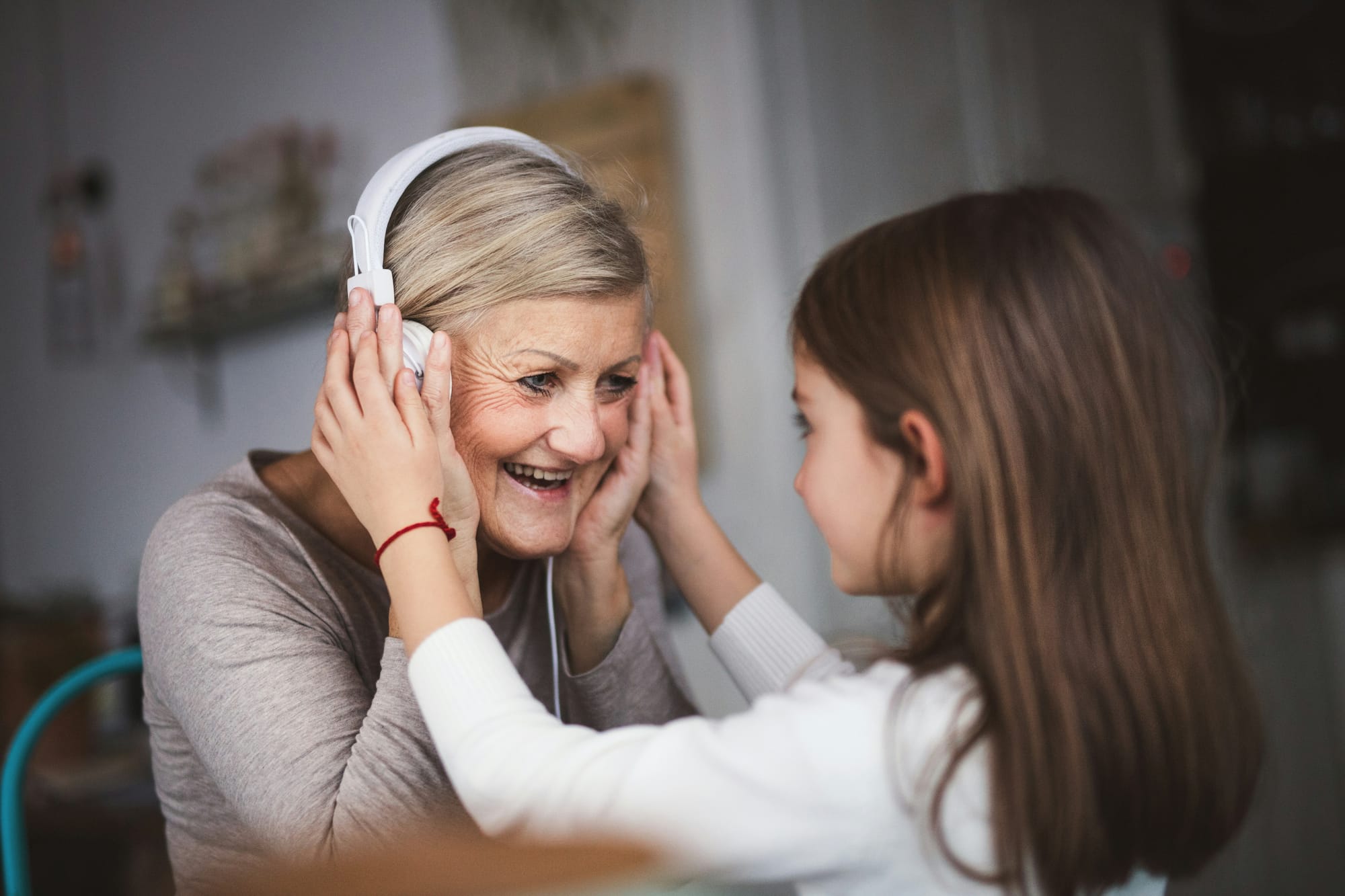 A young girl shares her headphones with her grandmother. Both are smiling. 