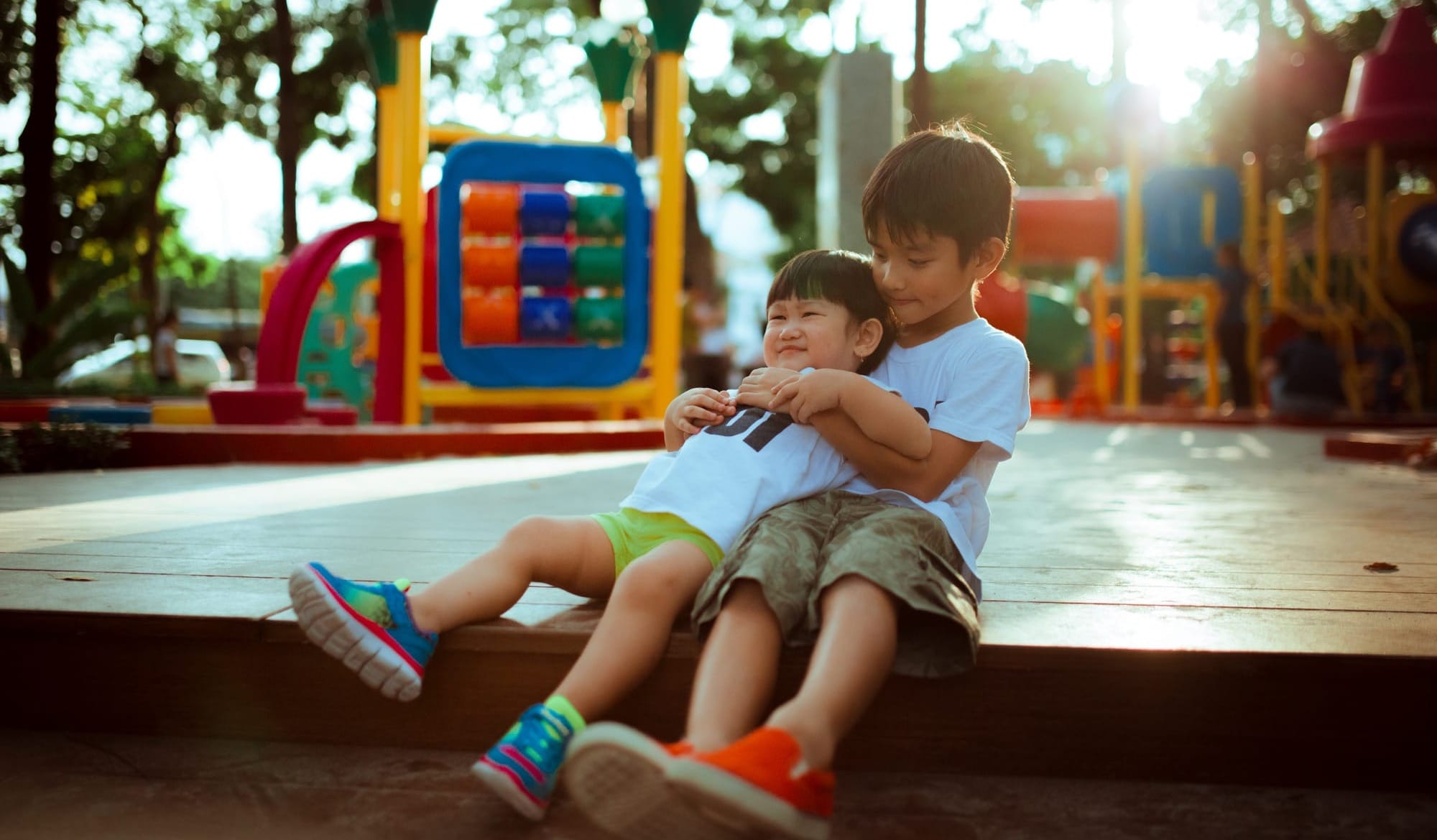 Two boys on a playground. The older restrains the younger, but they don't appear to be upset.