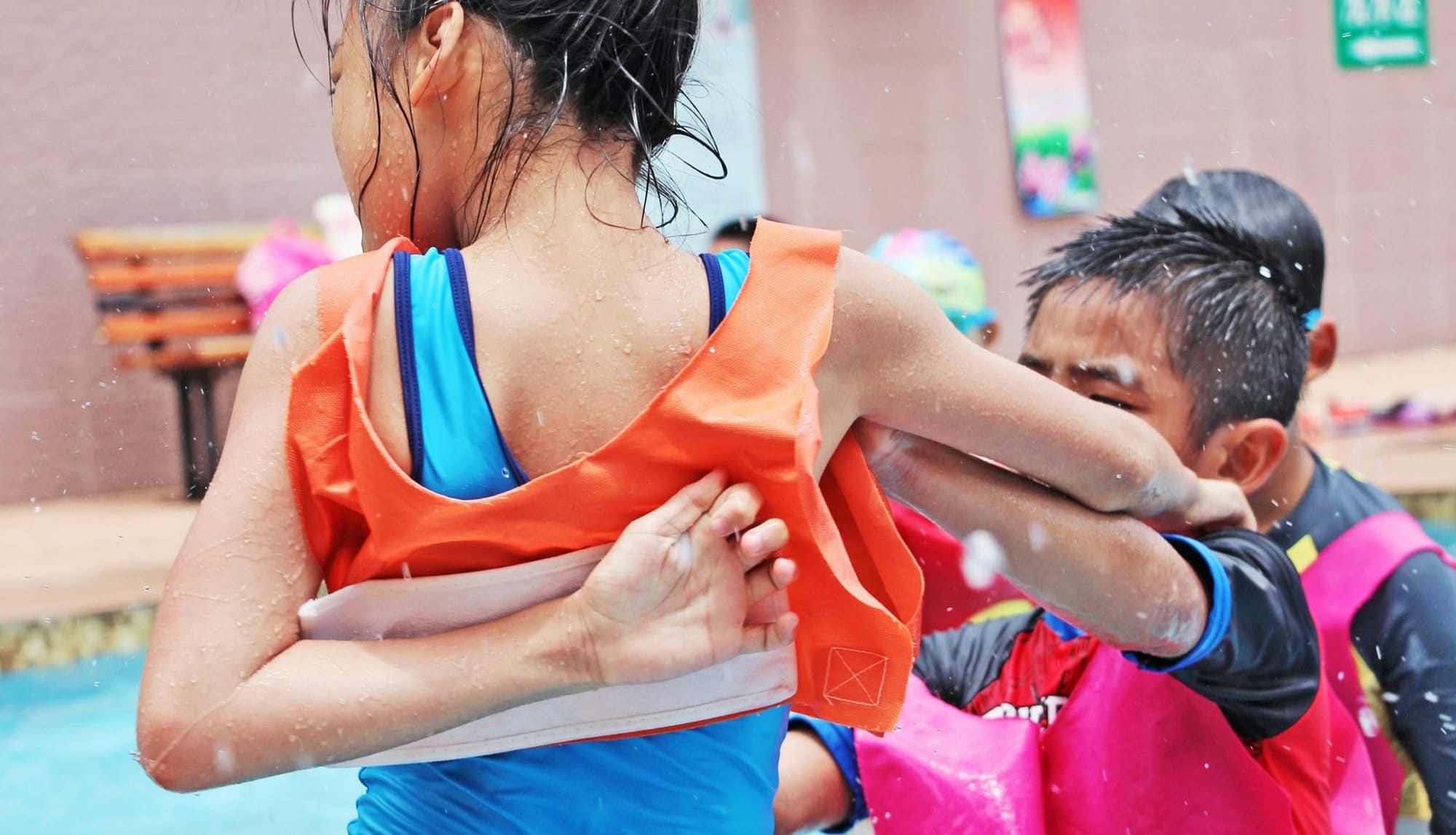 In a wading pool, a young boy pushes a girl a few years older. 