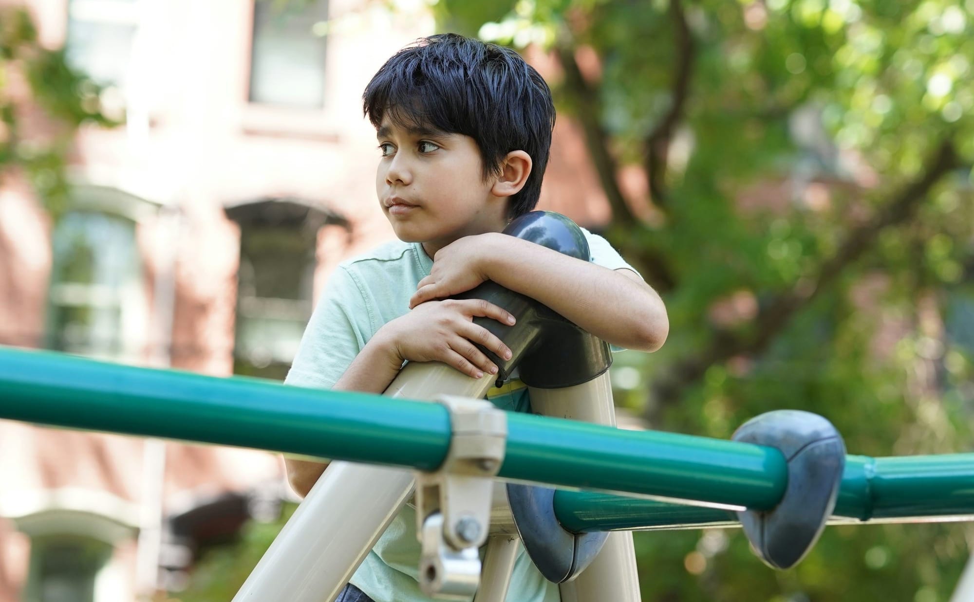 A boy climbing at a playground alone; he appears unhappy. 