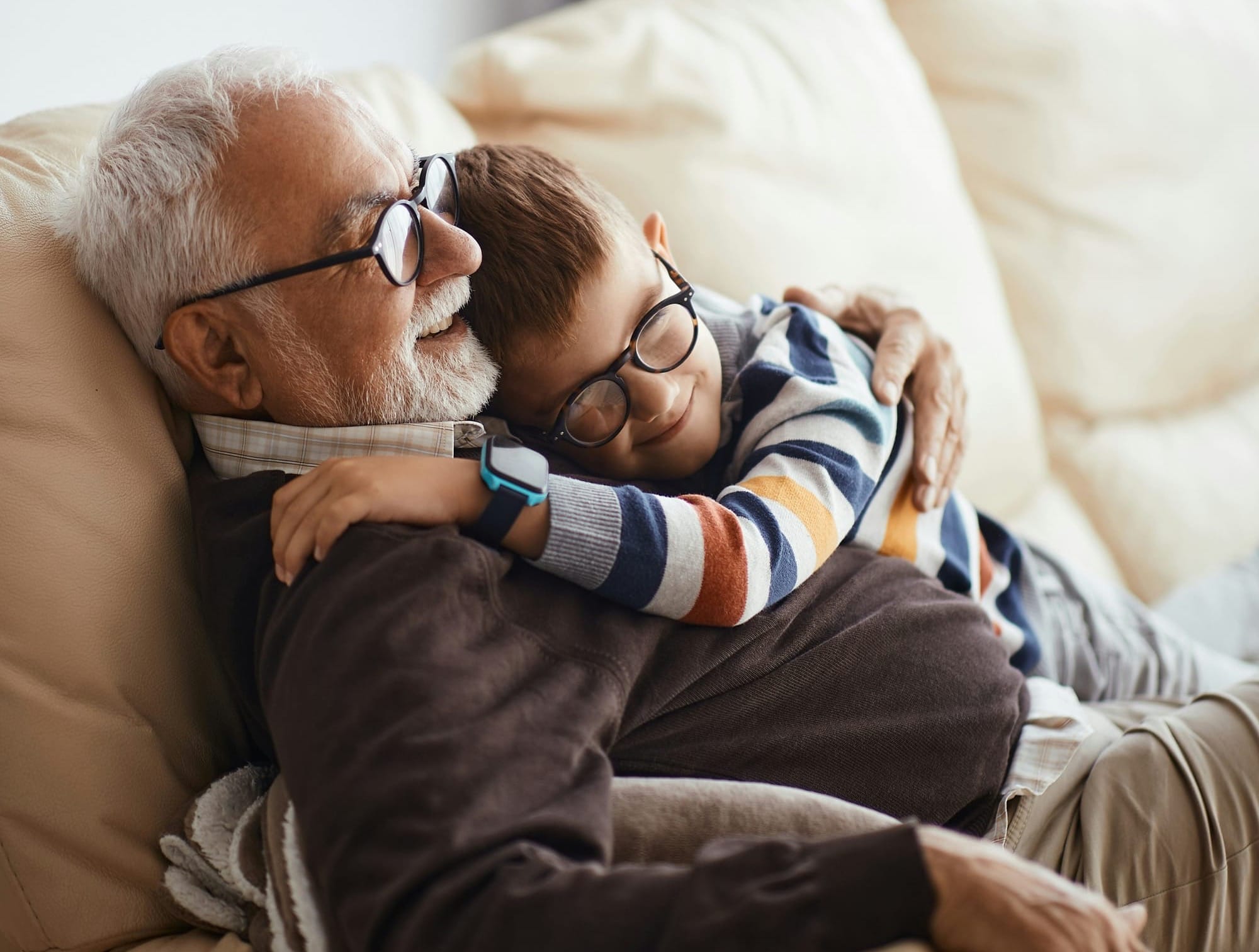A grandfather cuddles his grandson. They are wearing similar dark-framed eyeglasses.