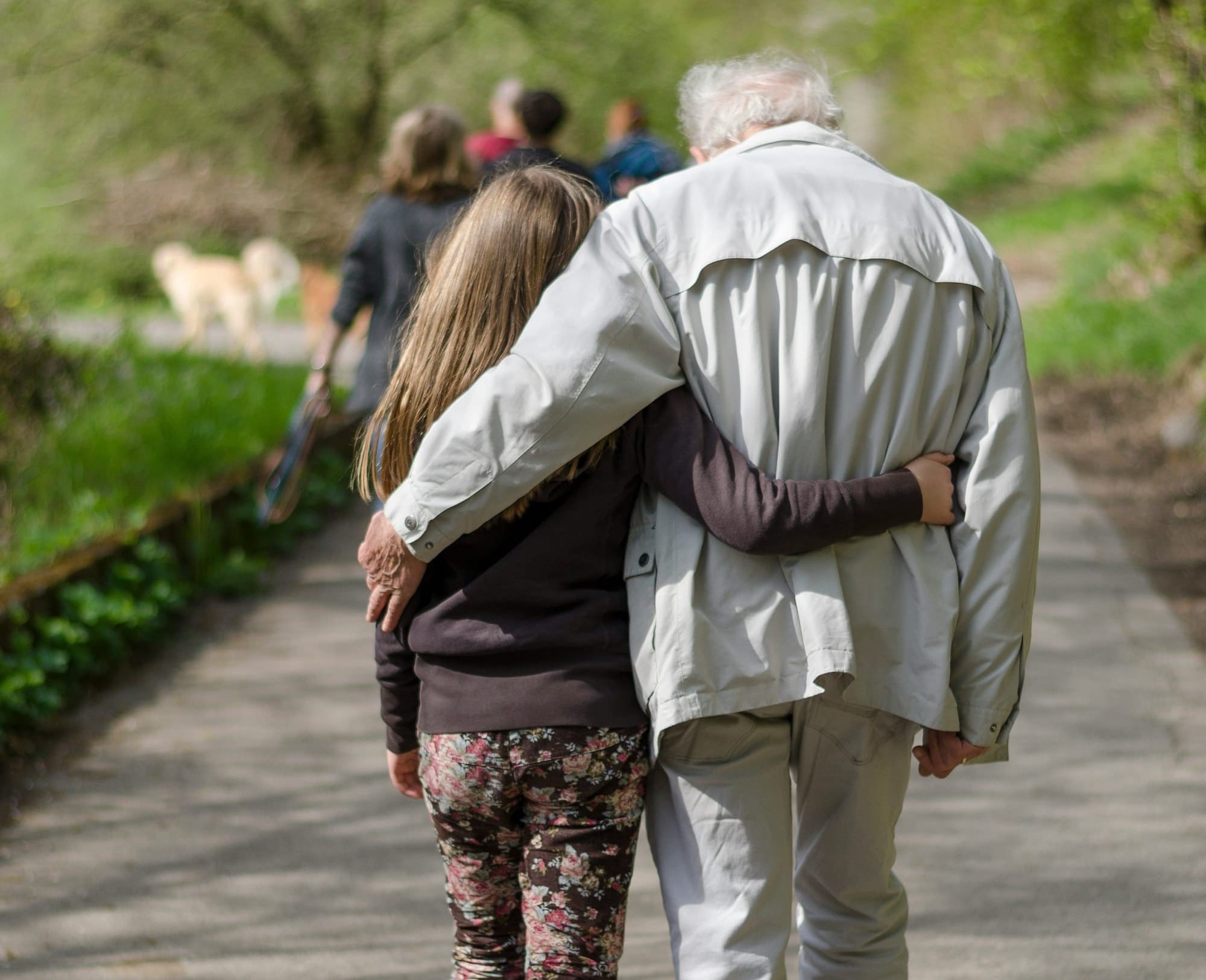 From behind, a grandfather and tween granddaughter with their arms around each other.