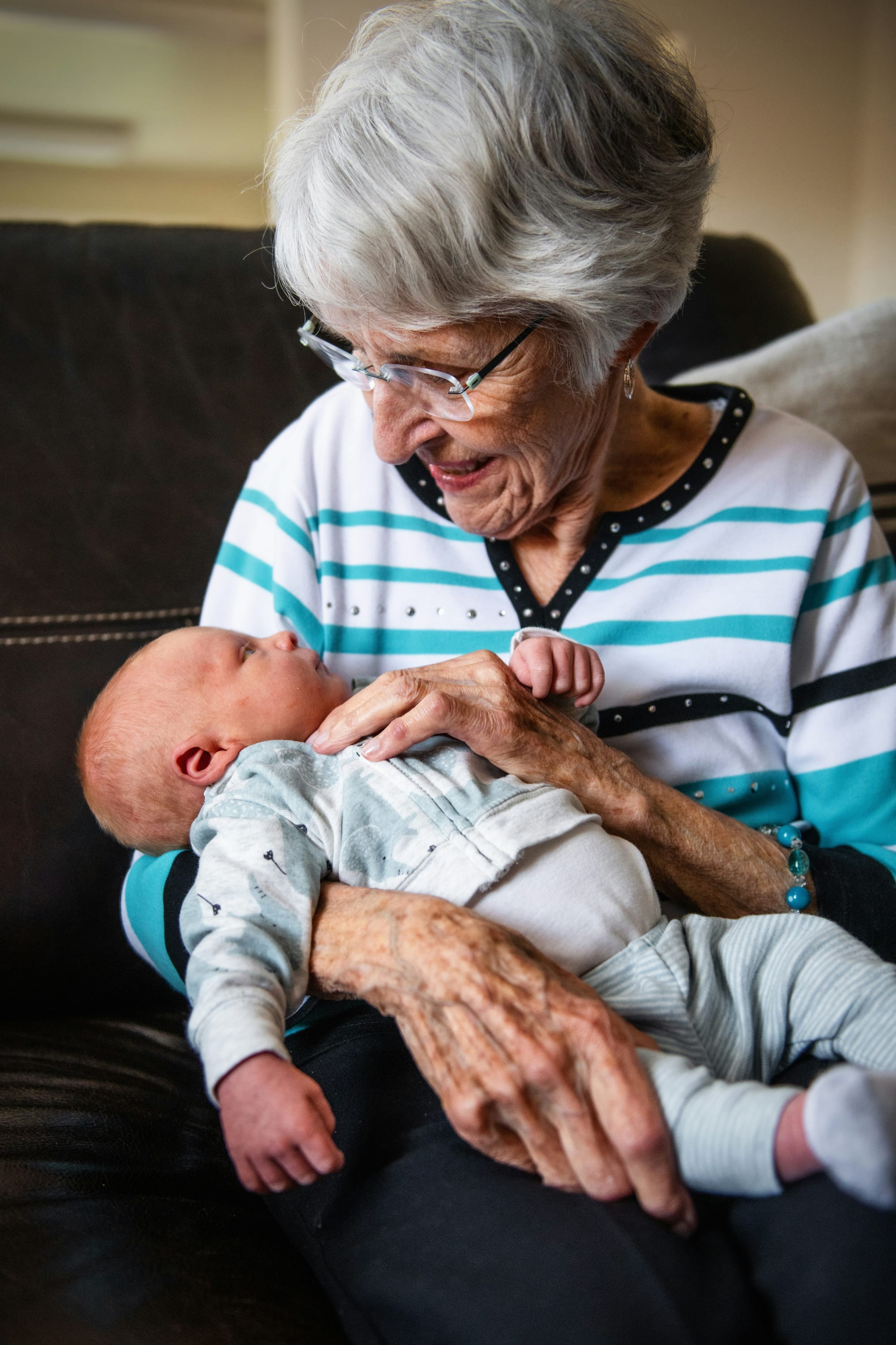 A smiling grandmother holds a weeks-old baby, getting eye contact. 