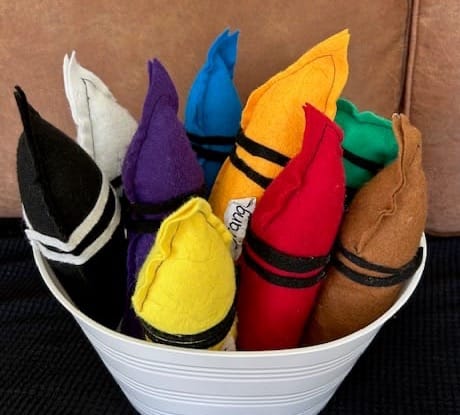 Stuffed felt crayon lookalikes in a bucket on a couch.