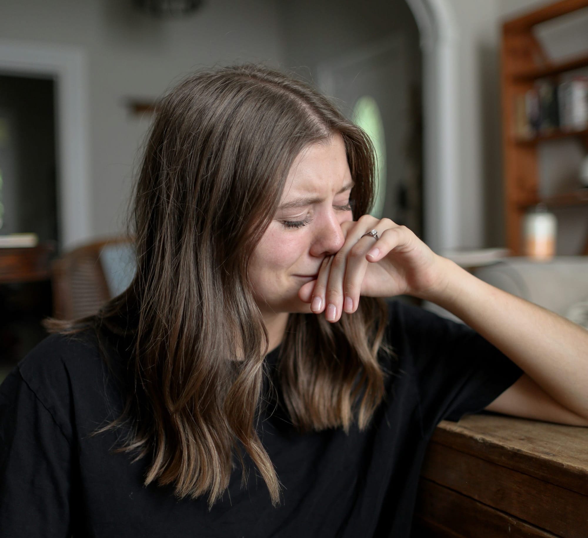 A woman at a table, hand at her face, near tears. 