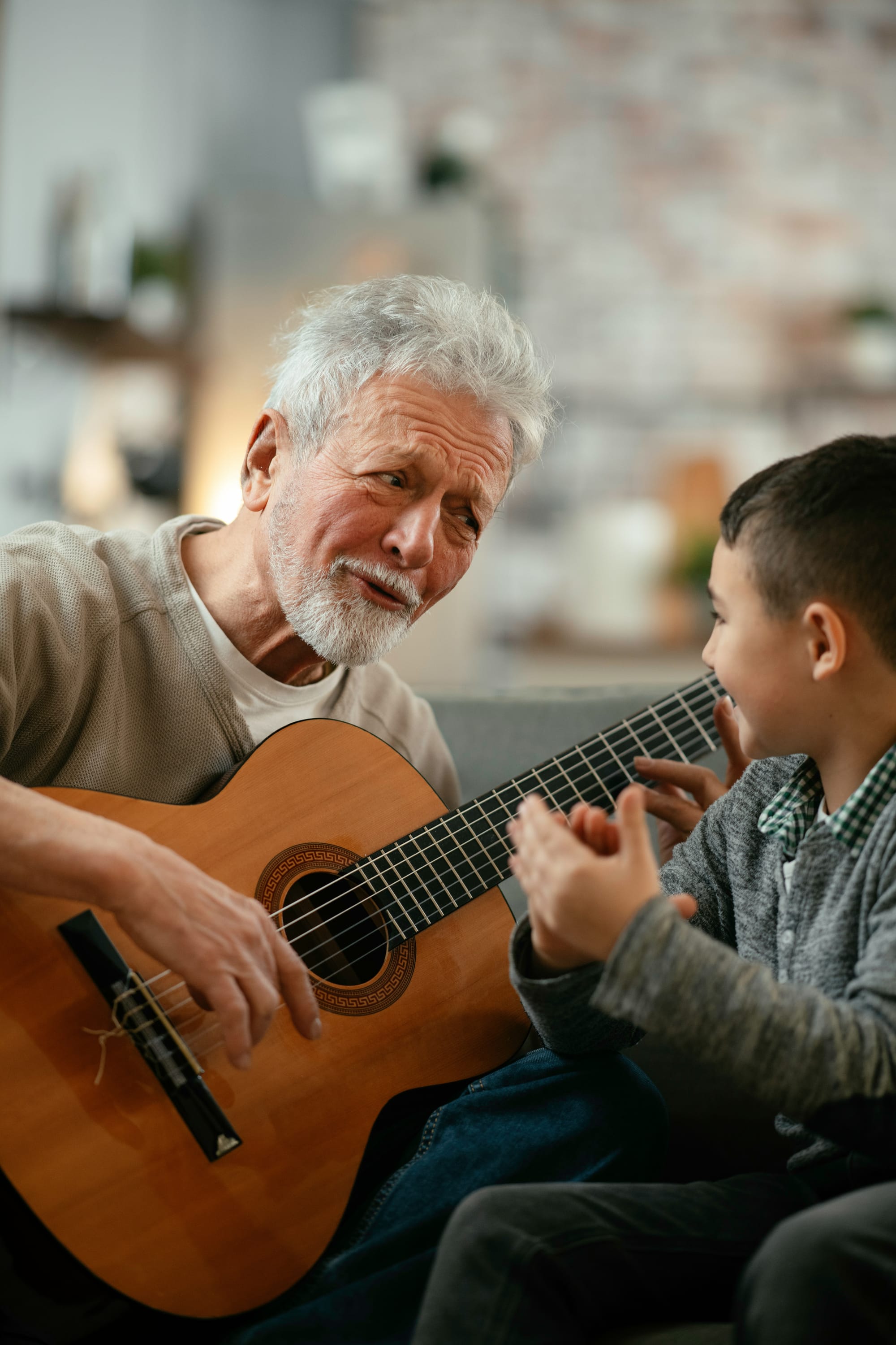 An older man plays guitar while a boy smiles and claps along.