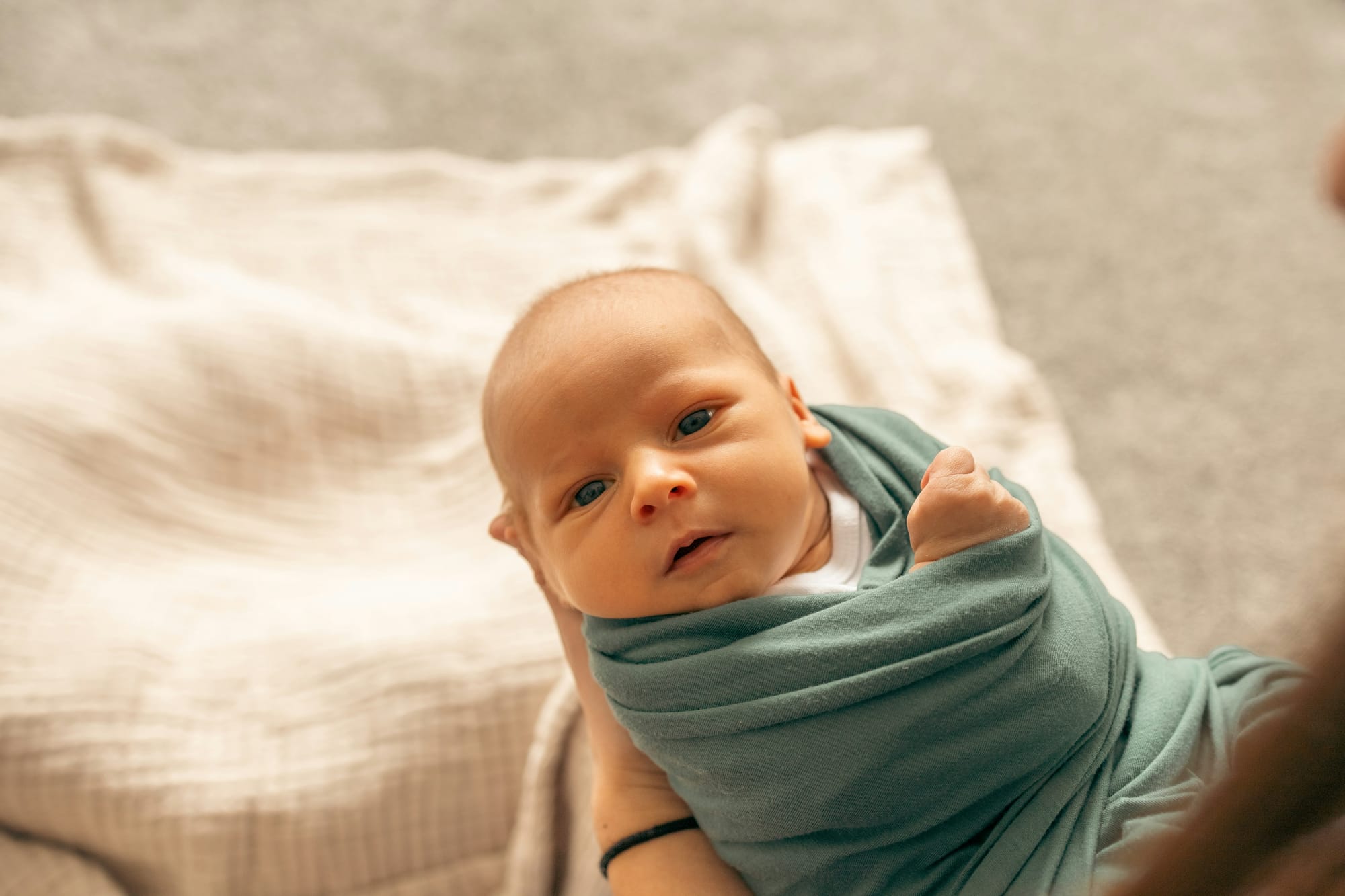 A mostly swaddled baby maybe a month old looks at the camera.