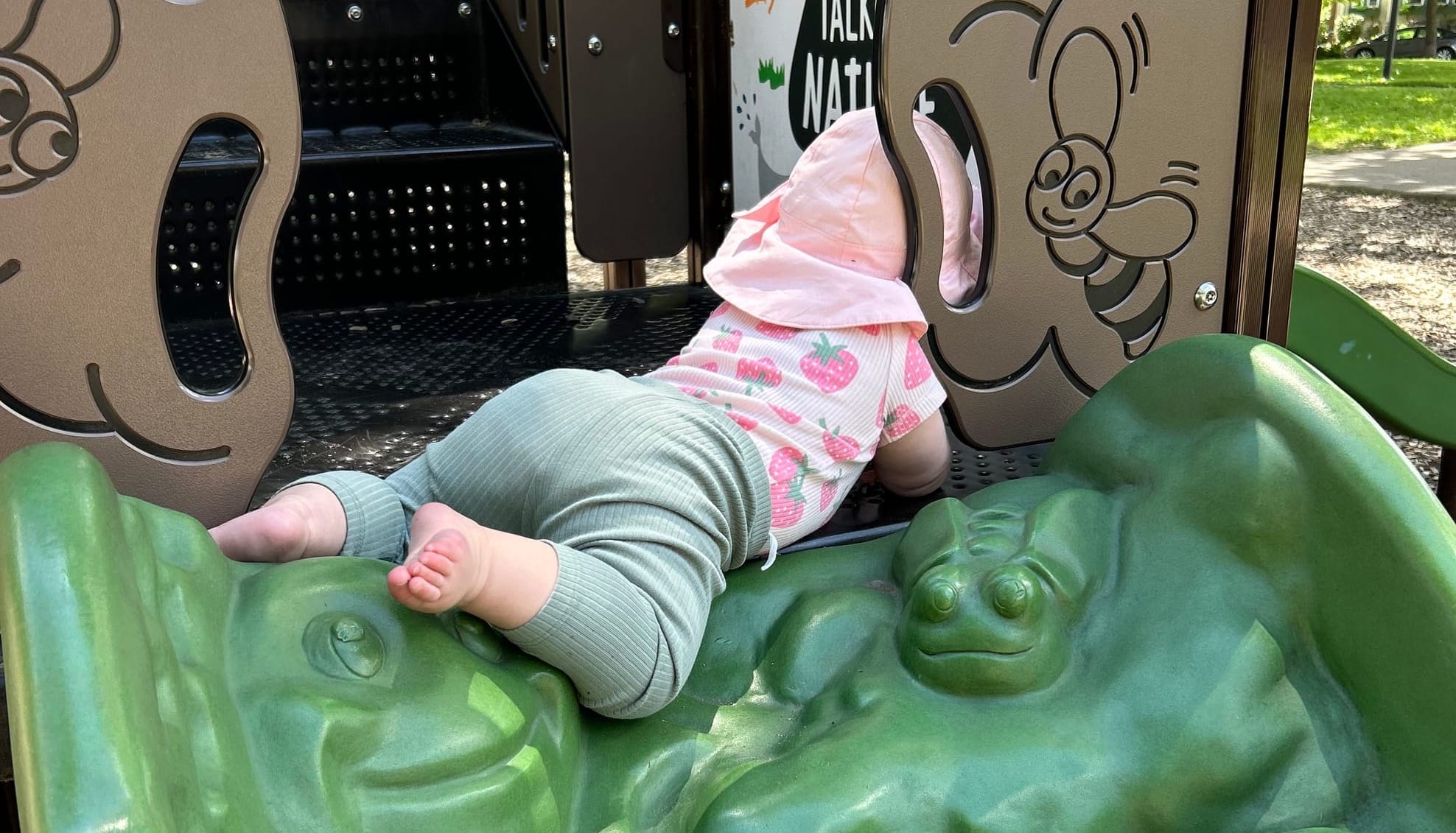 A baby plays on playground equipment at a park. 