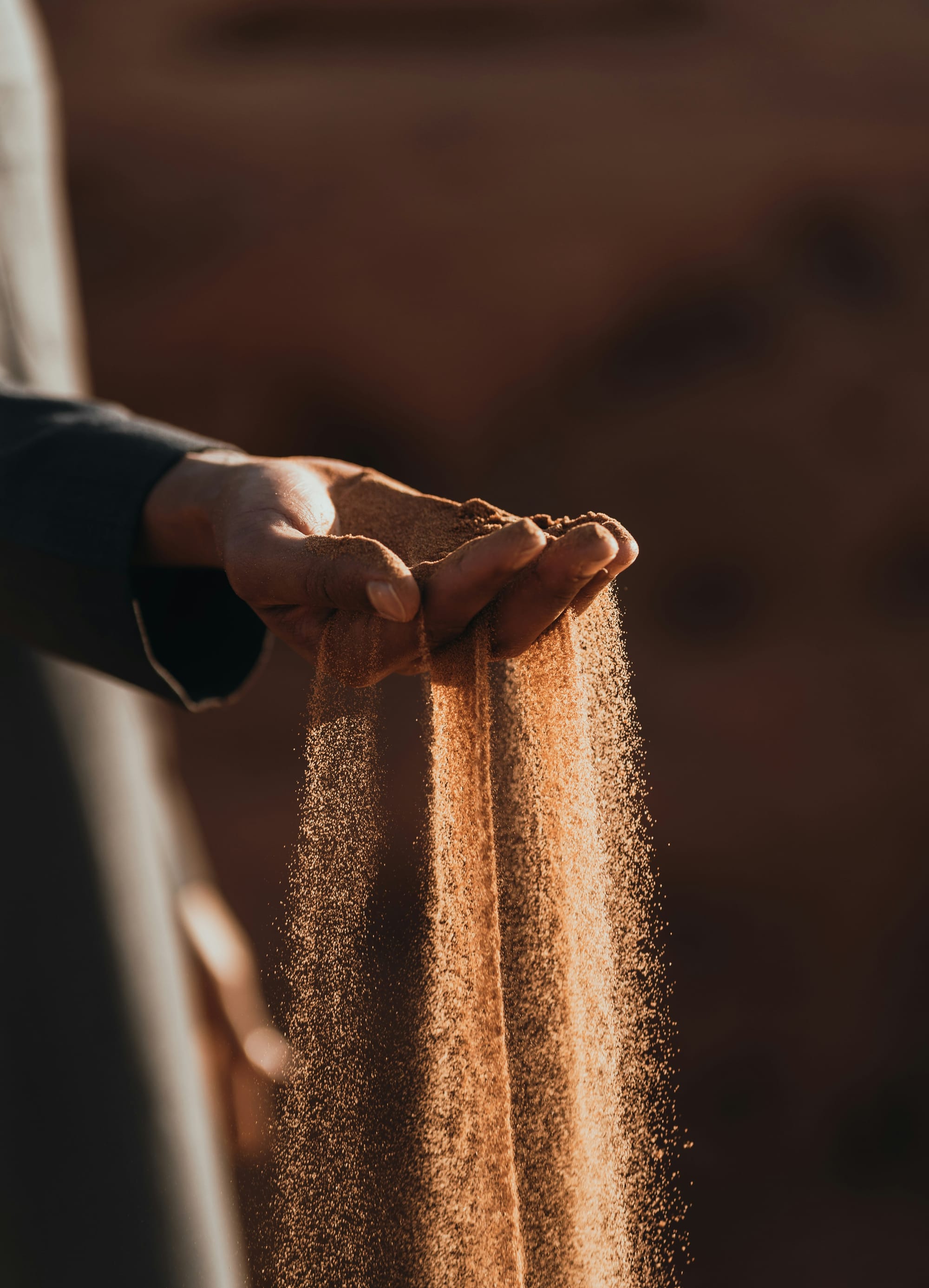 Sand, backlit by a bright light, runs through a person's fingers. 