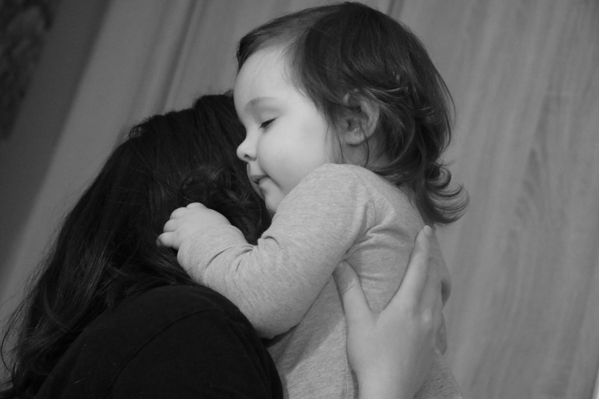 A woman hugs a baby or young toddler close. The woman's face is hidden, the baby's eyes are closed.
