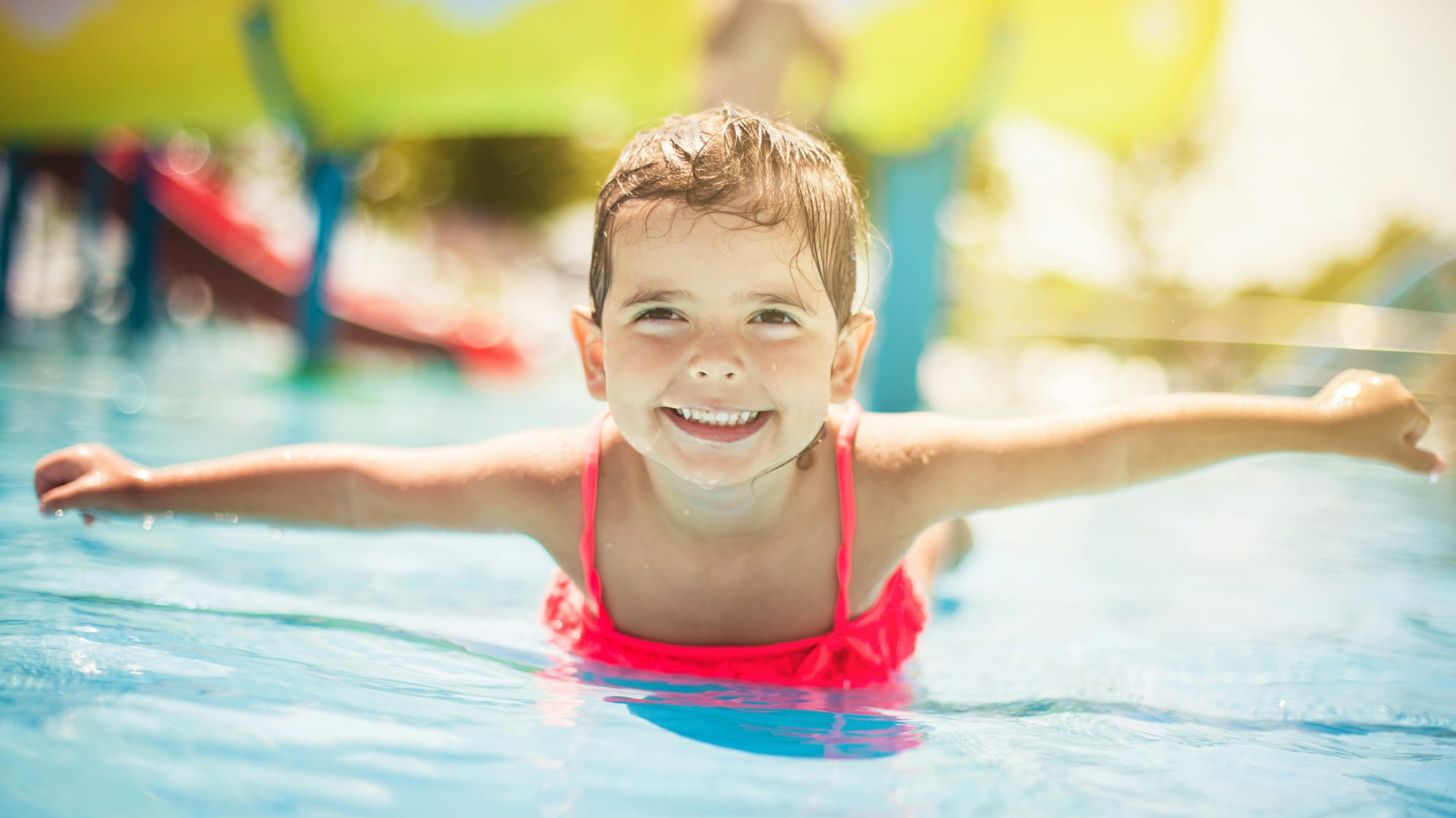 A smiling preschool-age girl wades in chest-high water.
