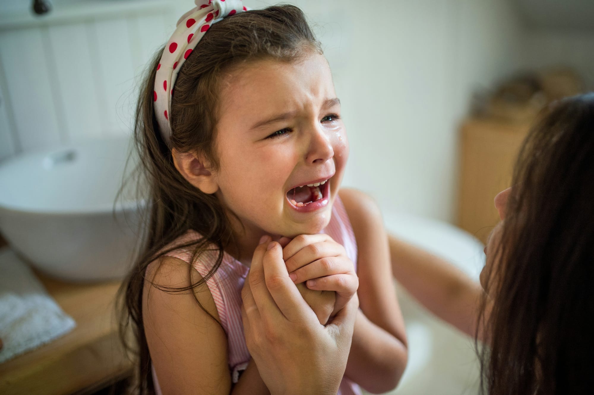 A little girl is tearful and very distressed. A woman in the foreground is comforting her.