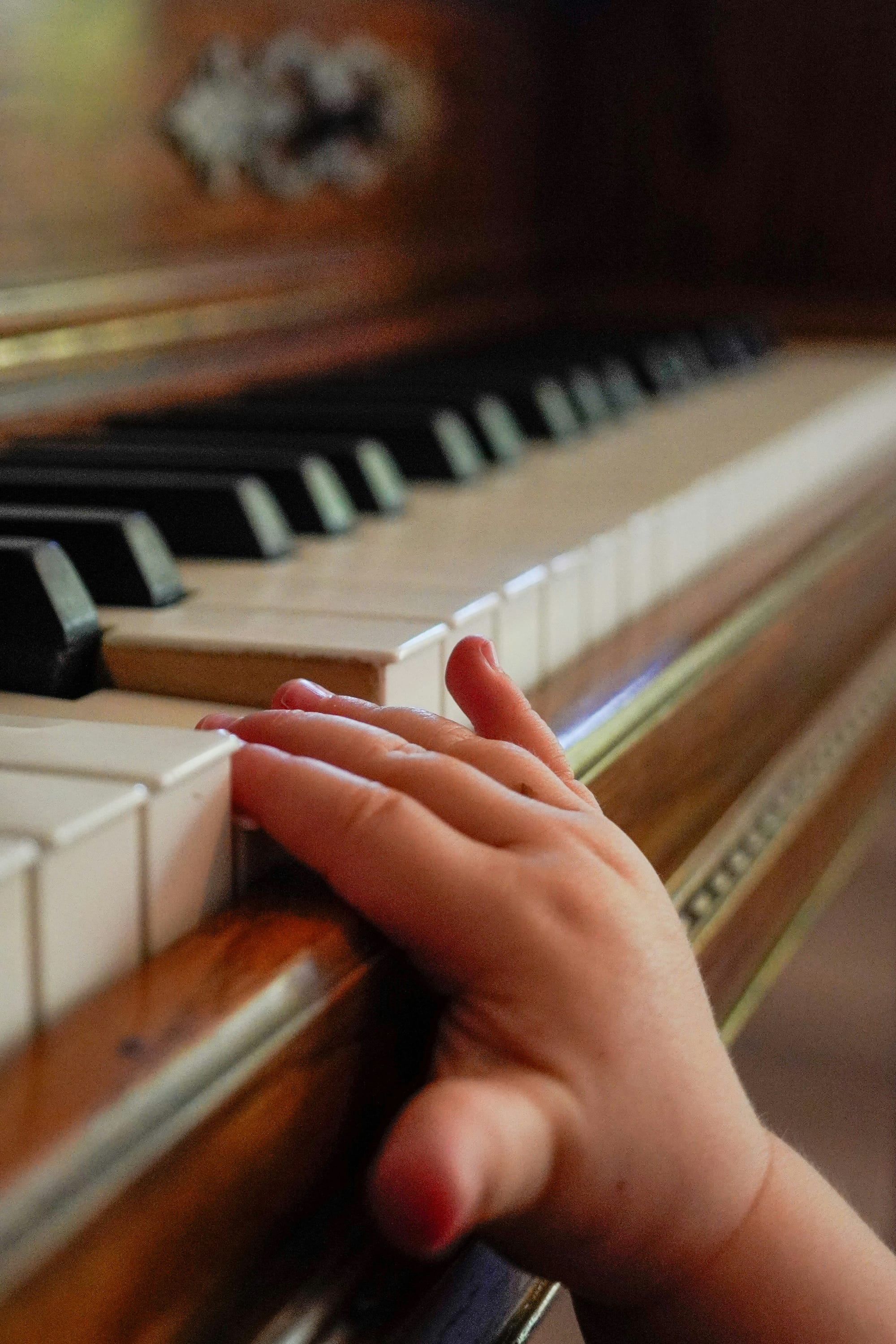 A baby's hand reaches up to push down white keys on a piano.