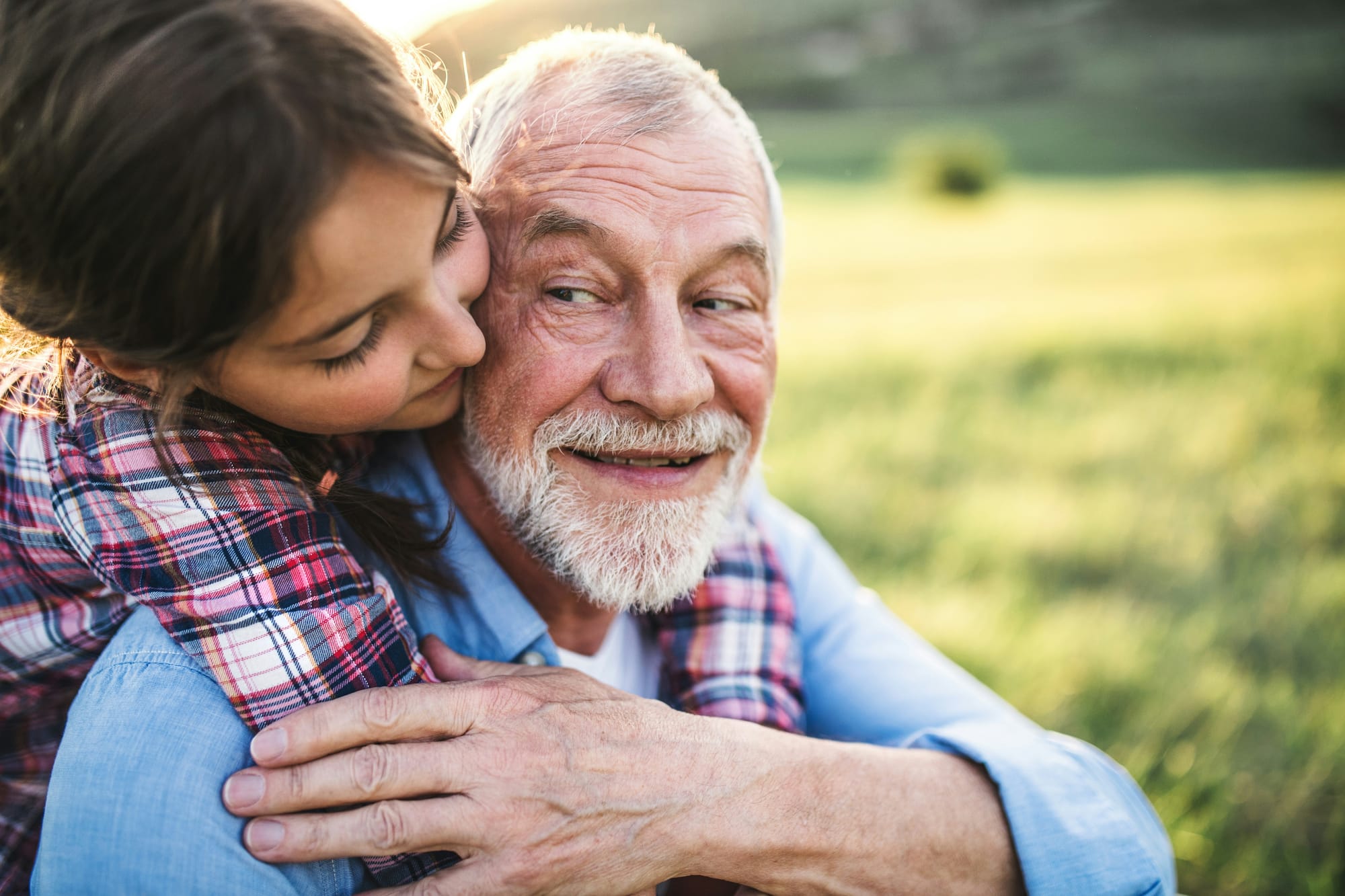 A girl wraps her arms around her Grandpa's neck; he looks back at her, smiling.