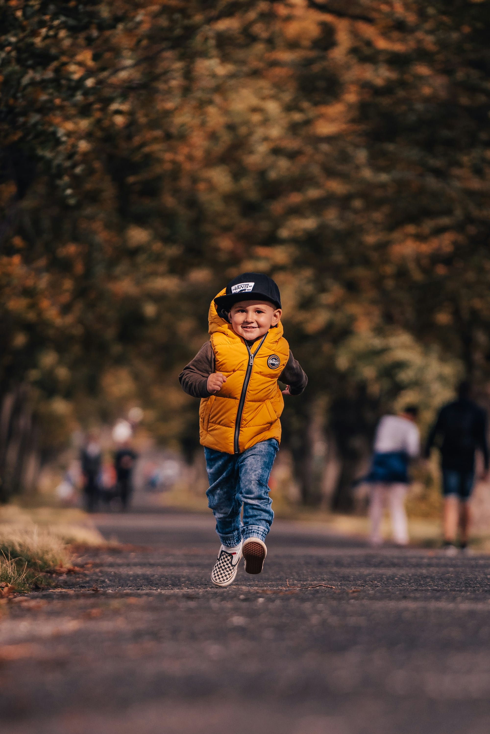 A boy in a marigold puffy vest runs, grinning.