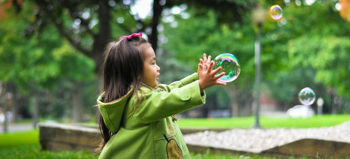 A young girl opens her hands to catch a soap bubble.