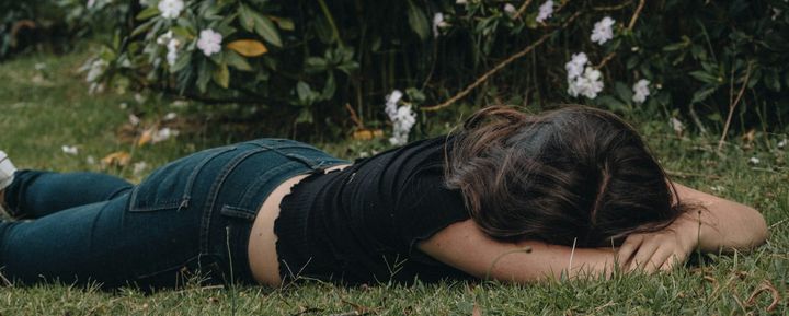 A girl lies face down in the grass. The tones of the photograph are muted.