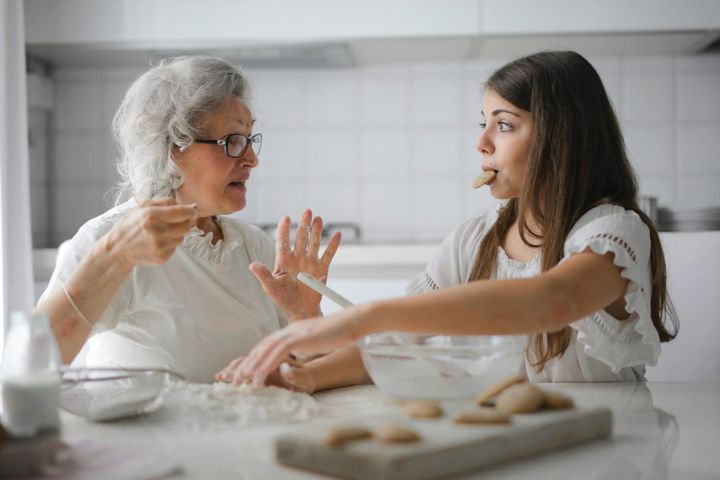 An older woman seems displease with a teen who has a cookie in her mouth and wide-eyed expression.