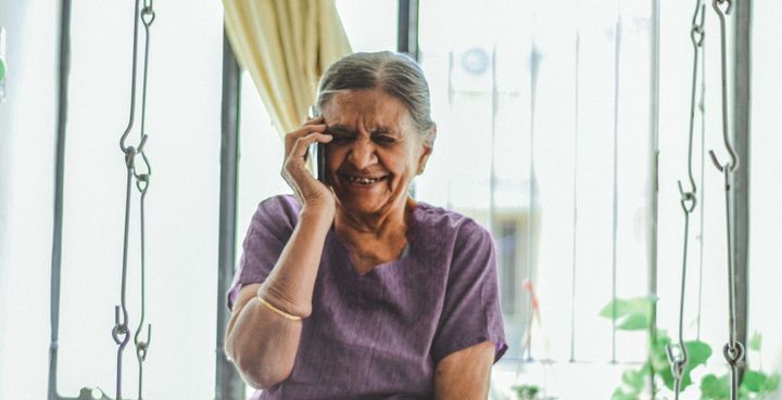 An older woman smiles while listening on a cellphone. 
