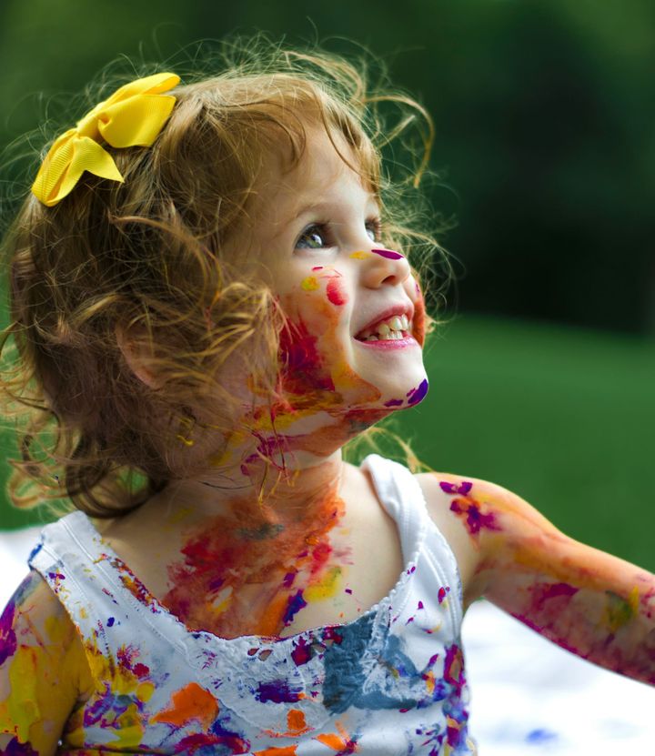 A young girl and her clothes covered in bright paint. 