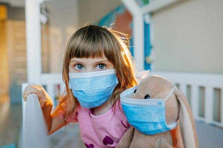 A young girl and her stuffed bunny both wearing medical face masks. 